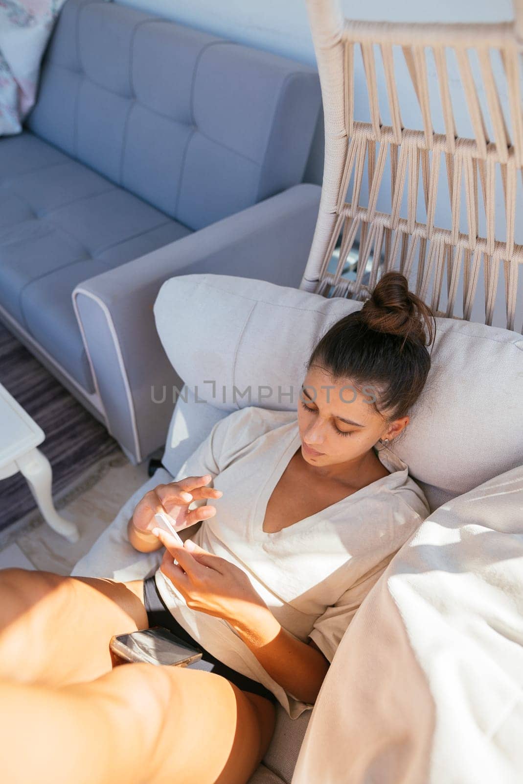 A woman lounges comfortably on a sofa, focused on her phone, embodying relaxation and modern lifestyle.