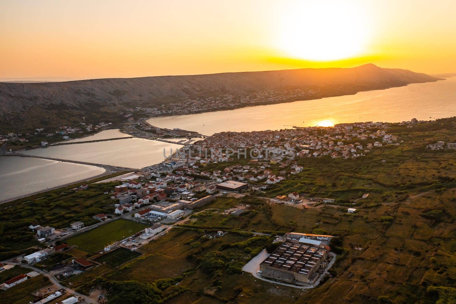 The landscape displays salt pans filled with seawater, surrounded by lush greenery at sunset