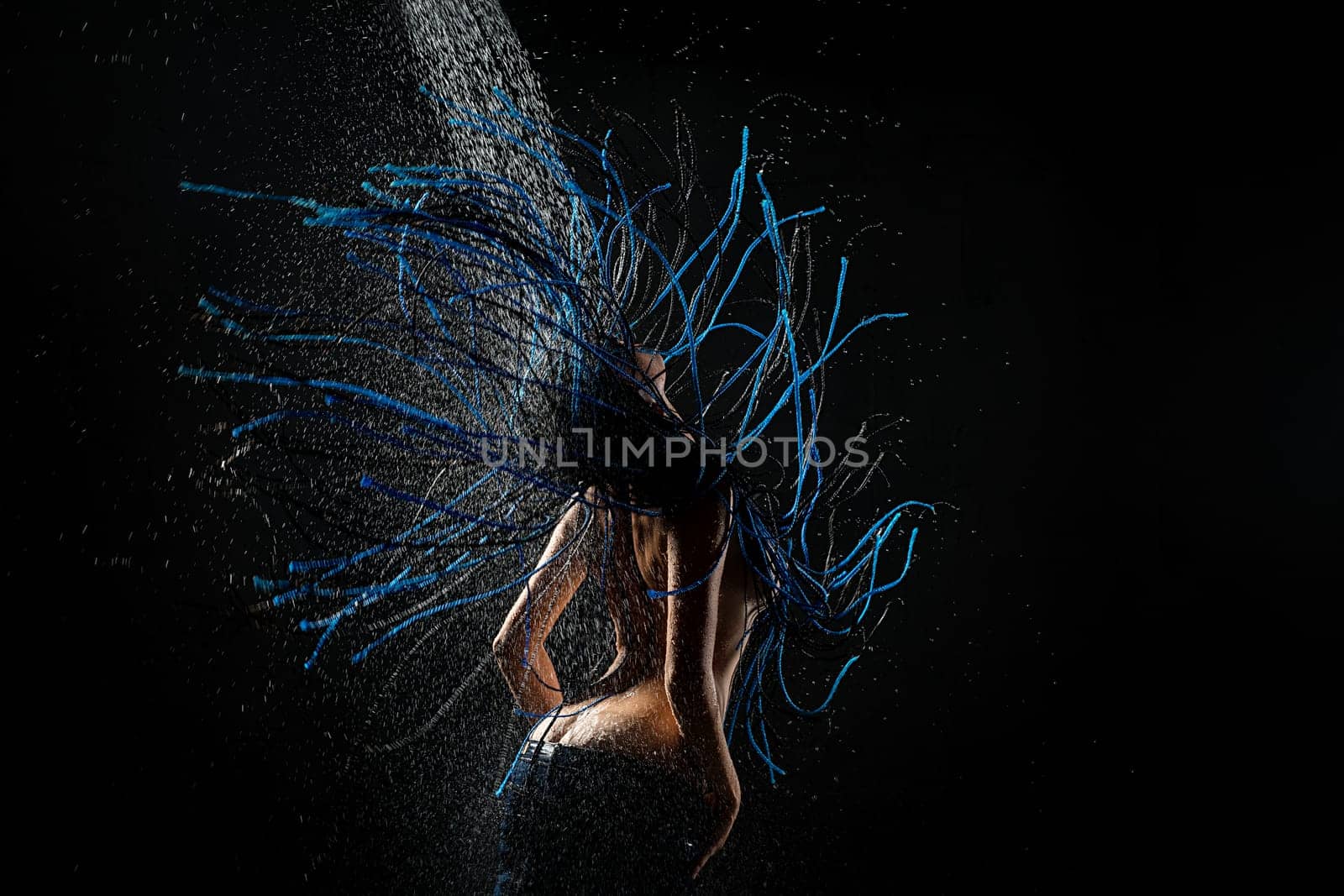 Brunette with blue dreadlocks topless having shower against black wall rearview shoot