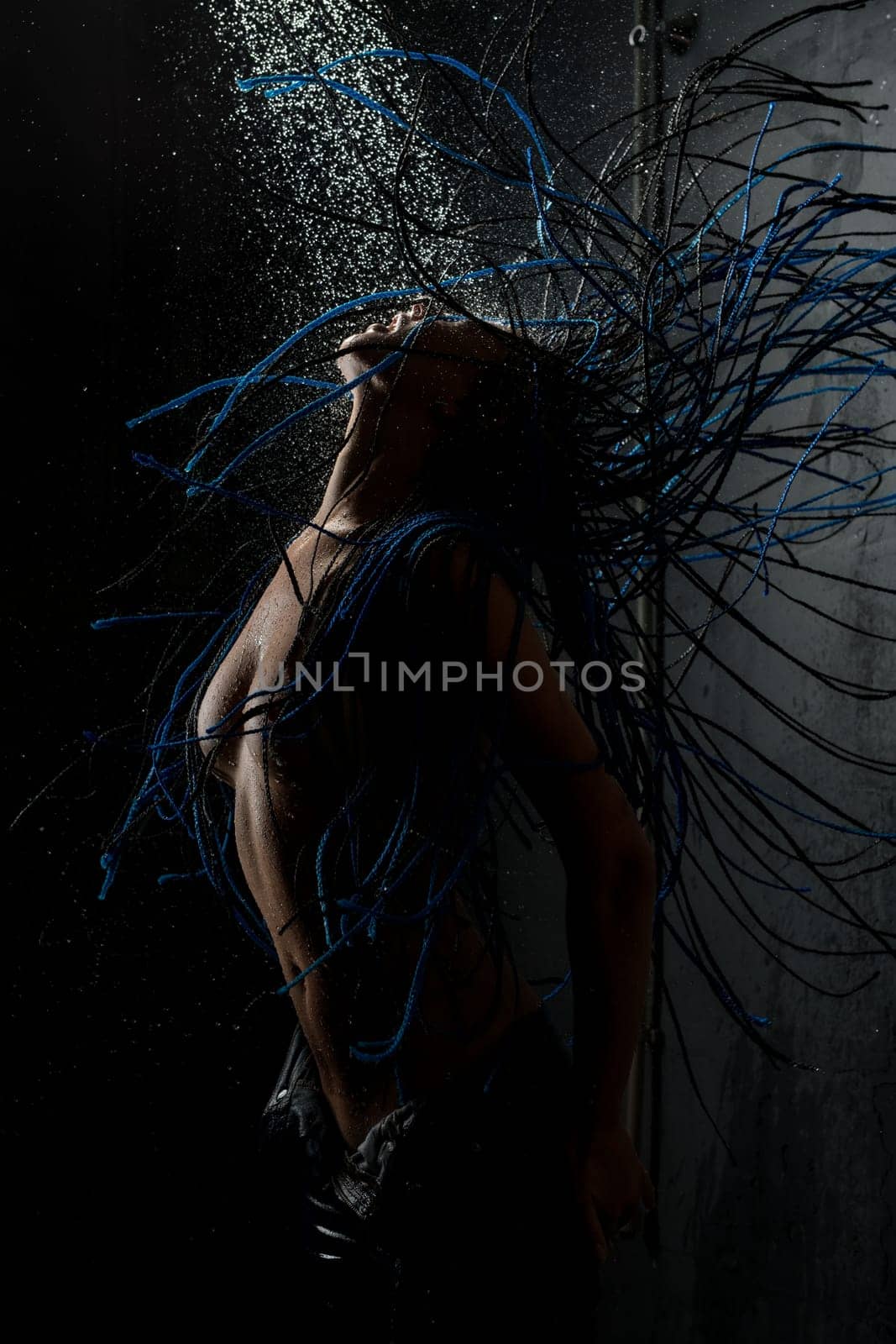 Brunette with blue dreadlocks topless having shower against black wall