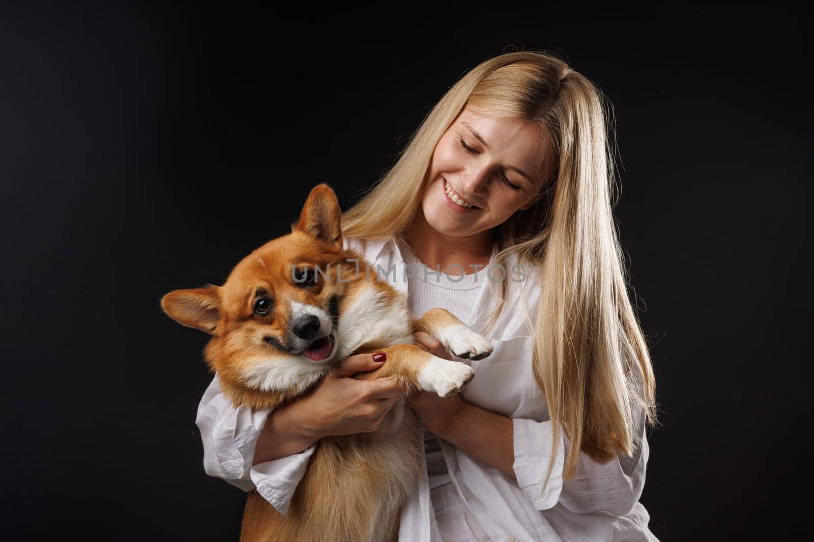 Woman holding and hugging happy corgi dog on black background. stylish concept. Love for dogs