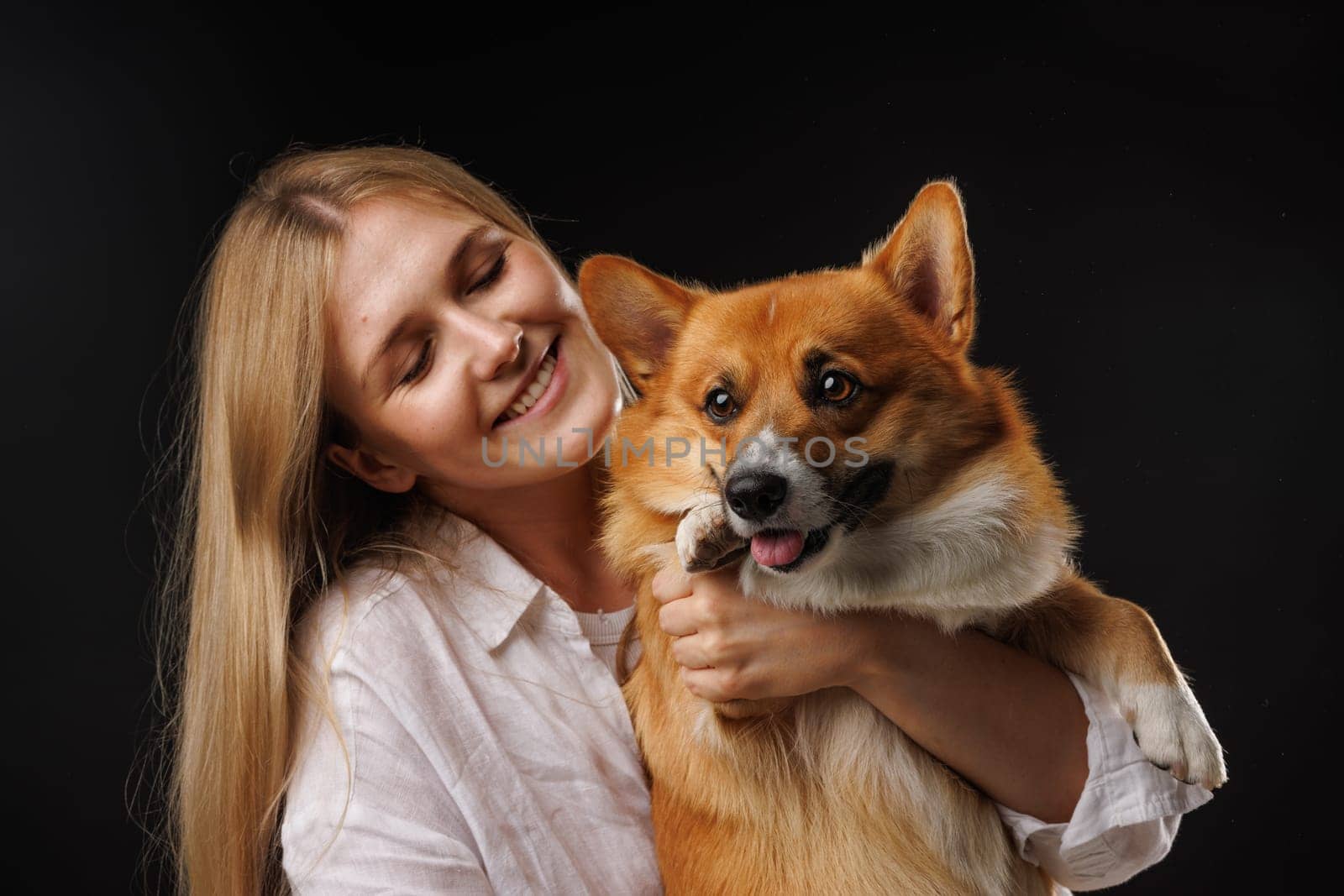 Woman holding and hugging happy corgi dog on black background. stylish concept. Love for dogs