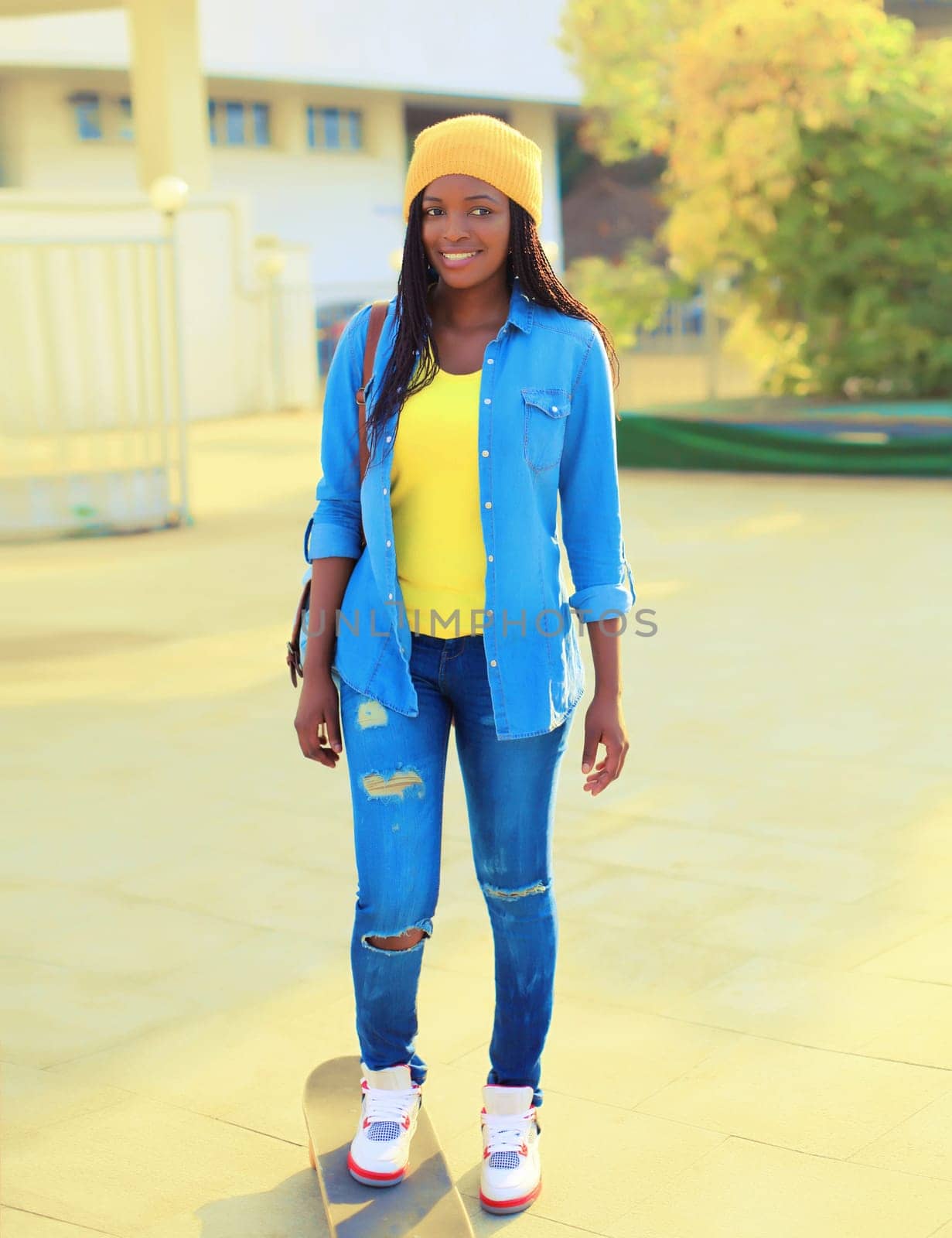 Stylish modern happy smiling young african american woman with skateboard in the city