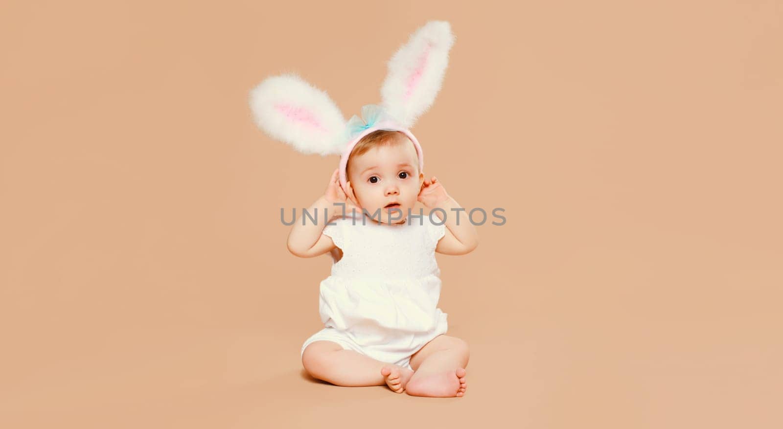 Portrait of cute baby with easter rabbit ears sitting on brown studio background