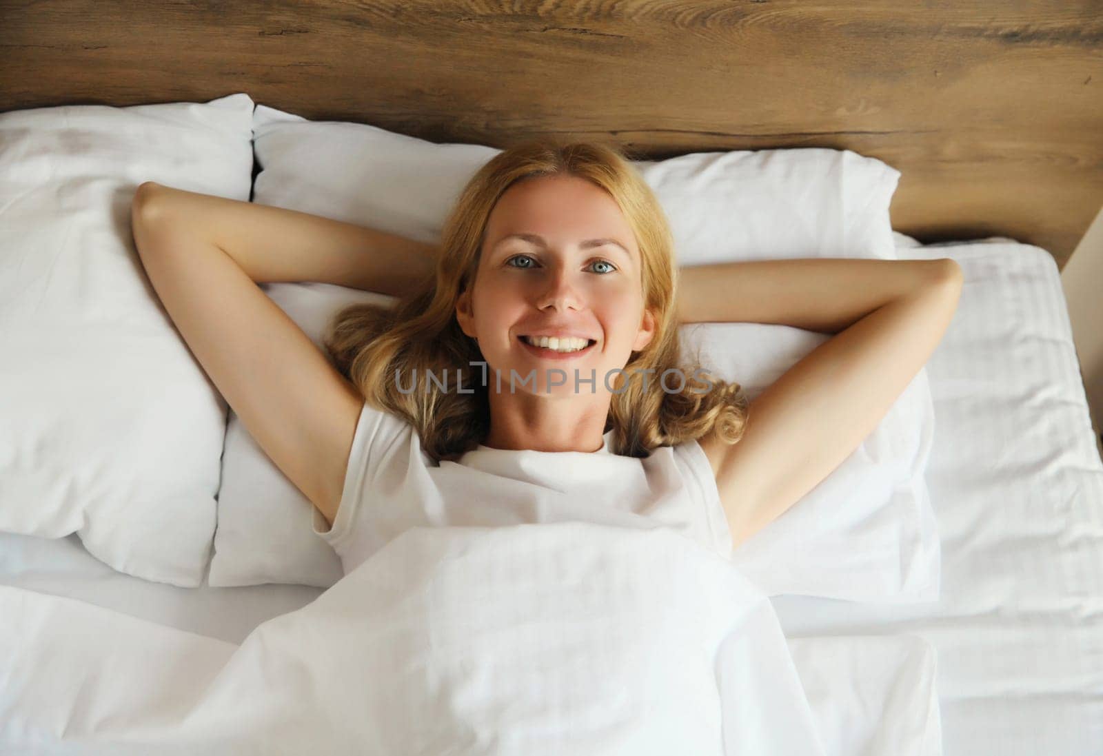 Happy young woman sleeping lying in bed on white soft comfortable pillow in bedroom at home