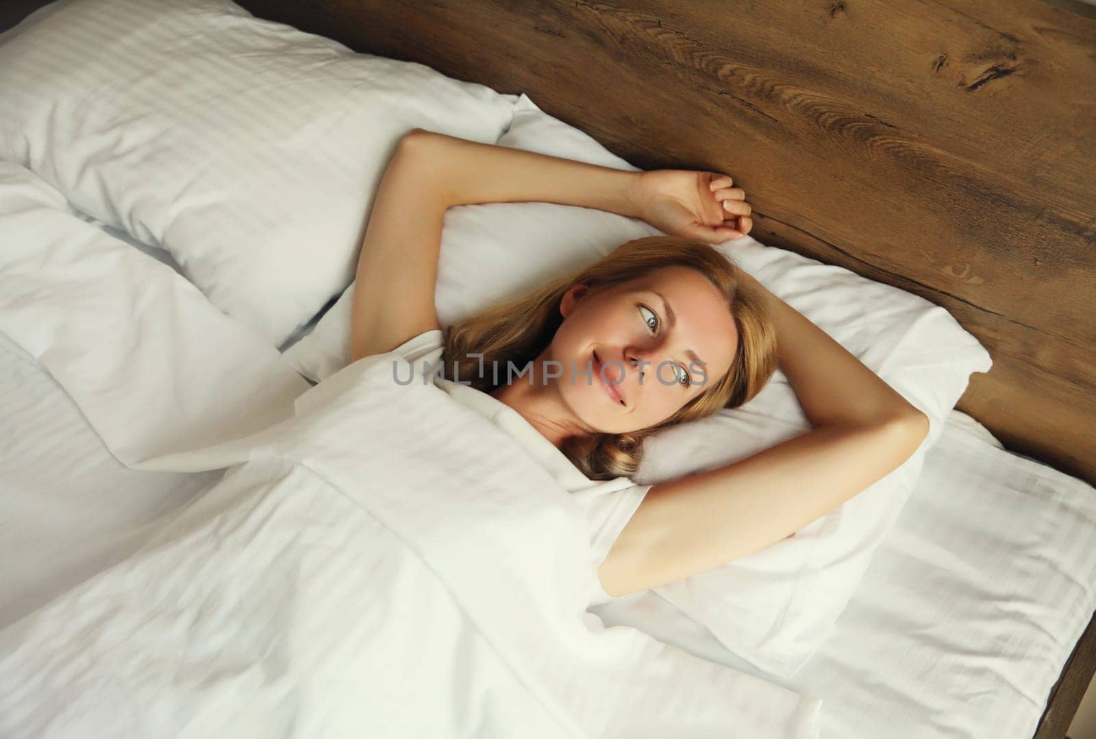 Happy young woman sleeping lying in bed on white soft comfortable pillow in bedroom at home