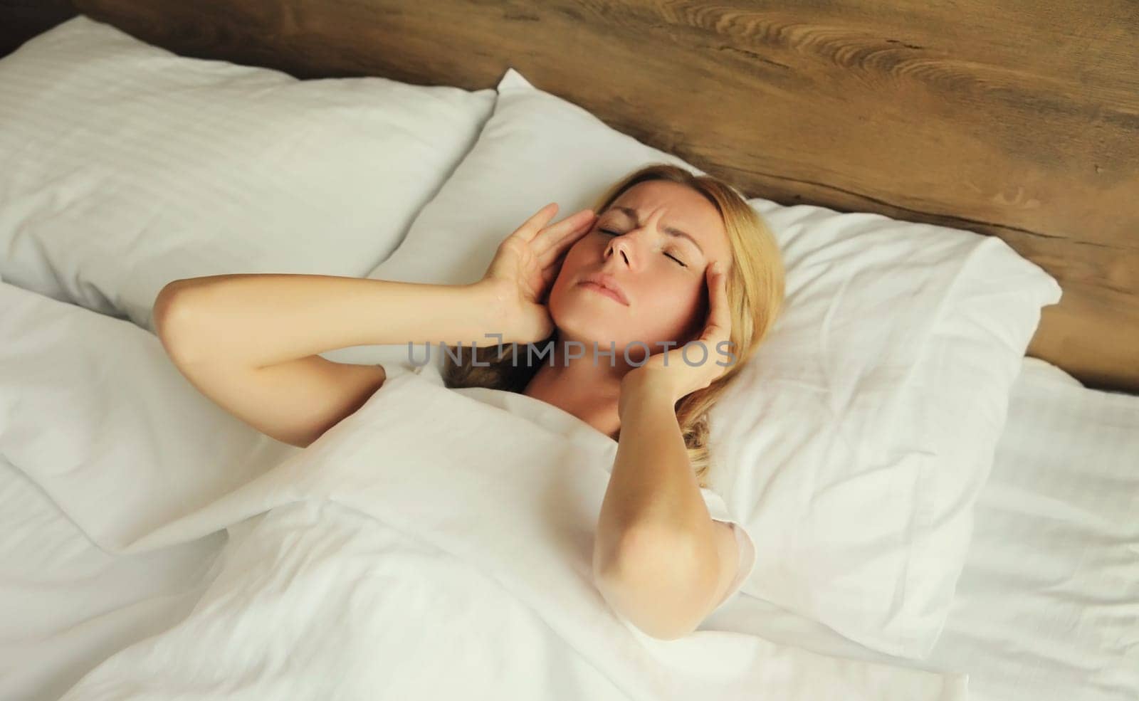 Upset exhausted woman with headache, pain tension in the head, suffers from migraine lying on the bed on pillow in bedroom at home