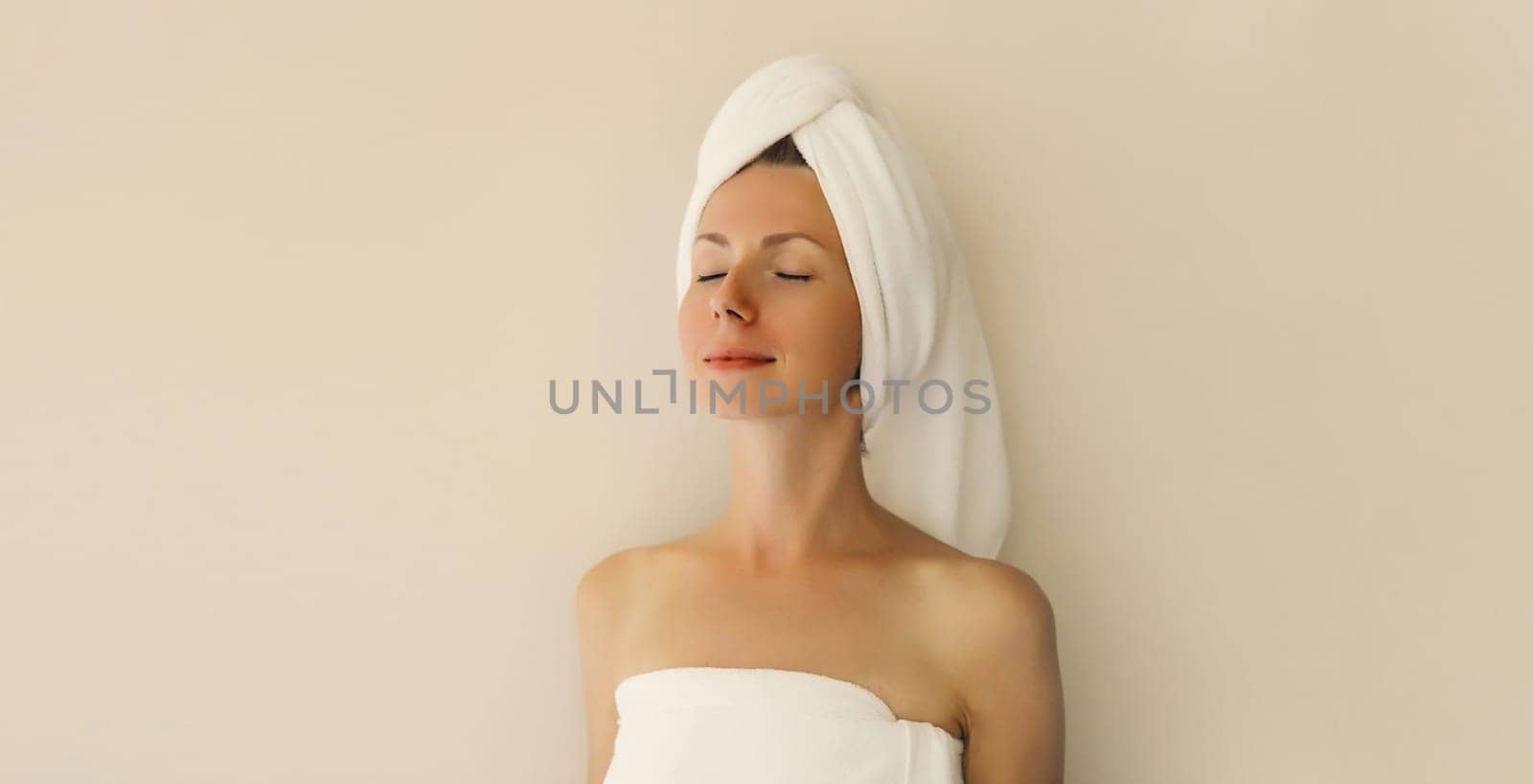 Natural beauty portrait of happy young caucasian woman enjoying her clean skin drying wet hair with white bath towel on her head