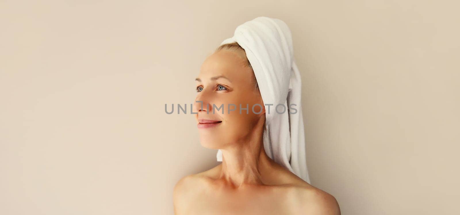 Natural beauty portrait of happy caucasian mature woman enjoying while drying wet hair with white bath towel on her head after shower in the morning at home