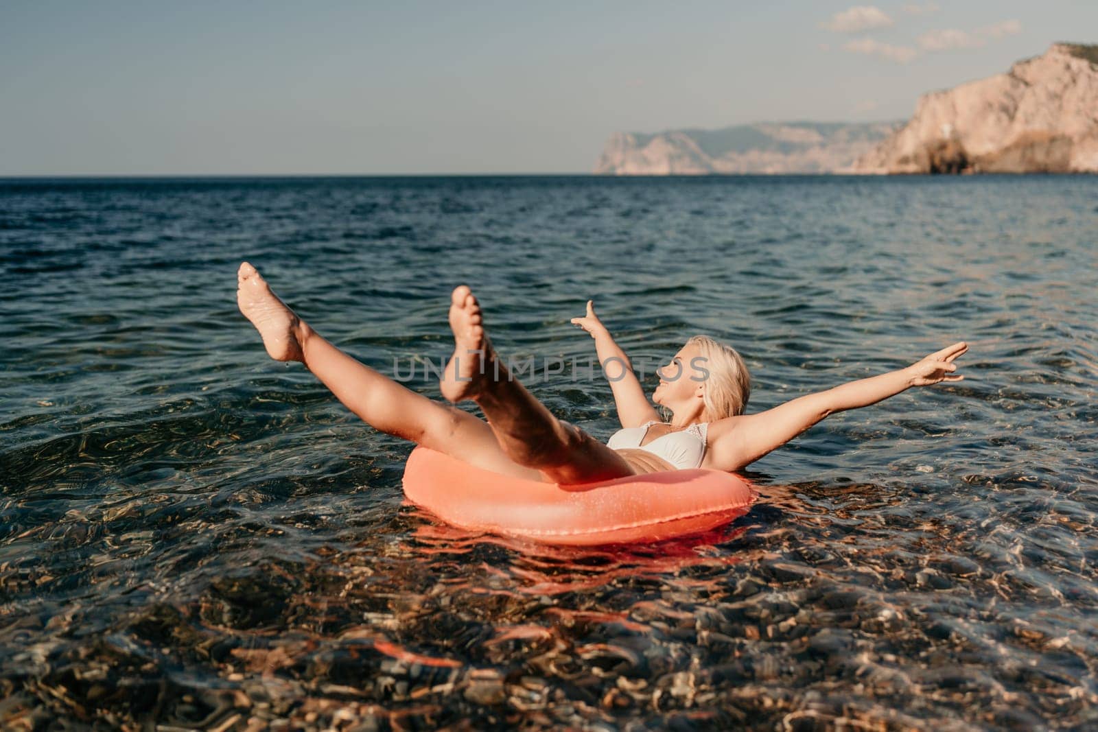 A woman is floating on a red inflatable raft in the ocean. She is smiling and enjoying the moment