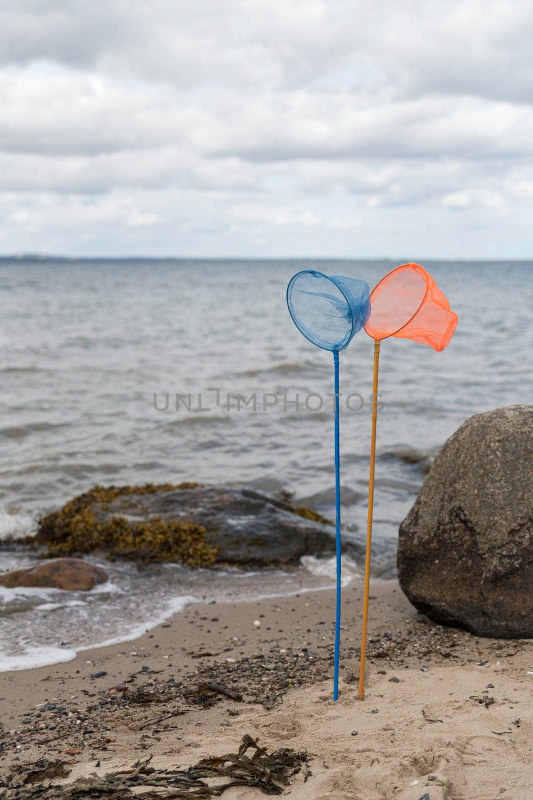 an orange and a blue fishing net on a pole standing on the beach with the sea and the horizon as a background in nature