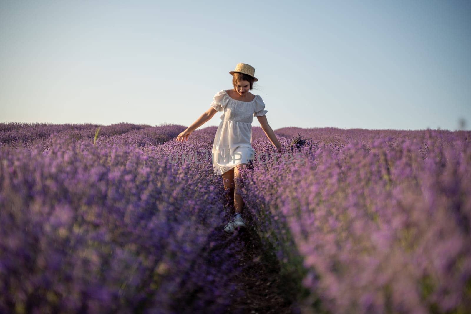 Lavender field happy girl in white dress with hat runs through a lilac field of lavender. Aromatherapy travel.