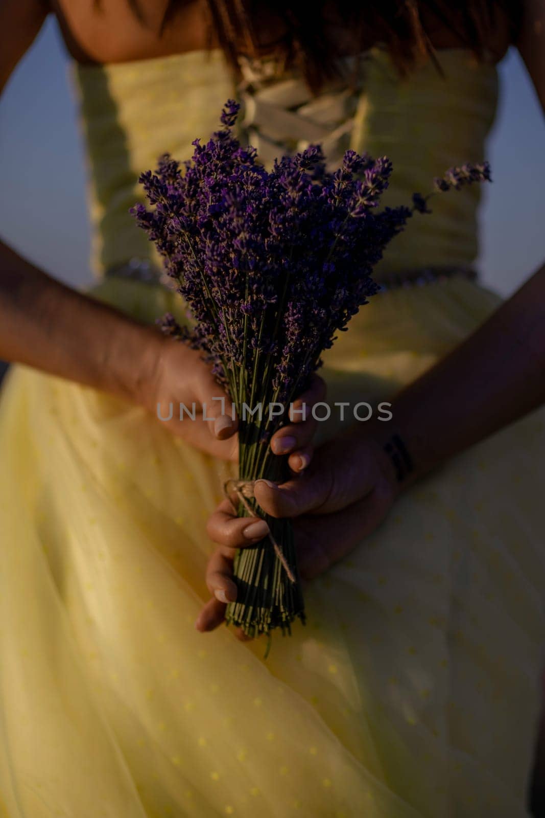 Woman poses in lavender field at sunset. Happy woman in yellow dress holds lavender bouquet. Aromatherapy concept, lavender oil, photo session in lavender.