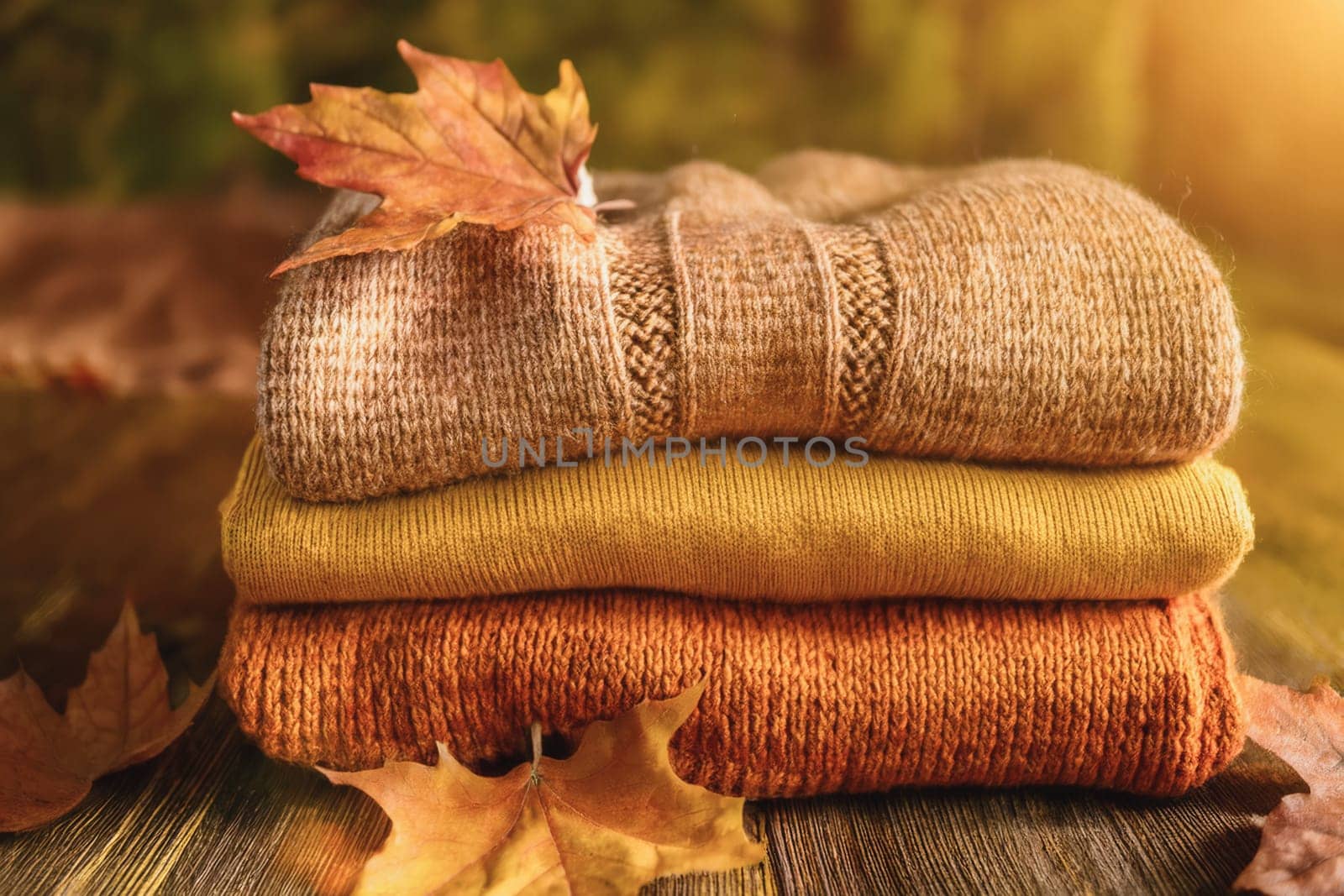 Stacked wool autumn sweaters on wooden background with leaves