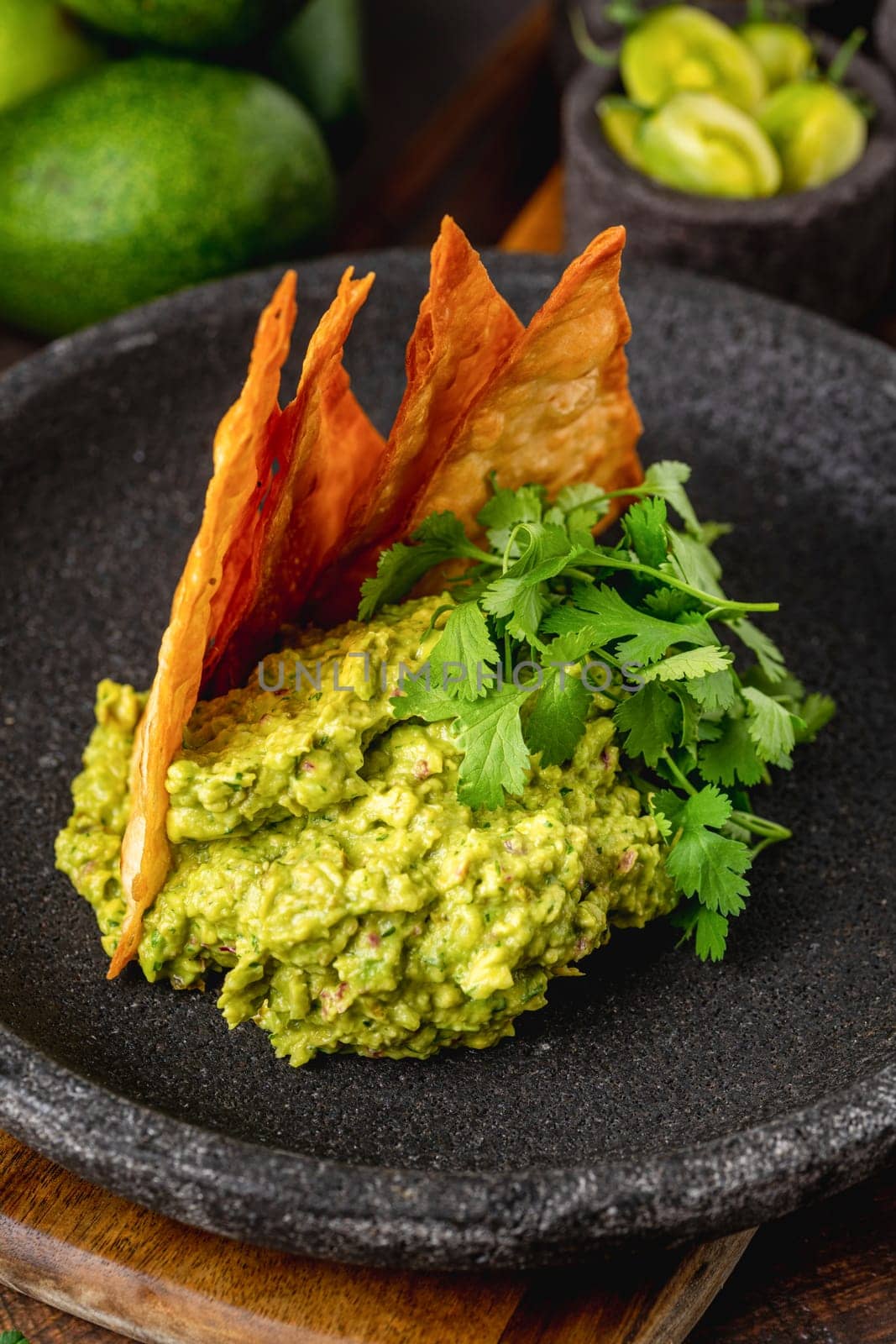 Avocado dip guacamole with crispy tortillas on black stone plate on wooden table by Sonat