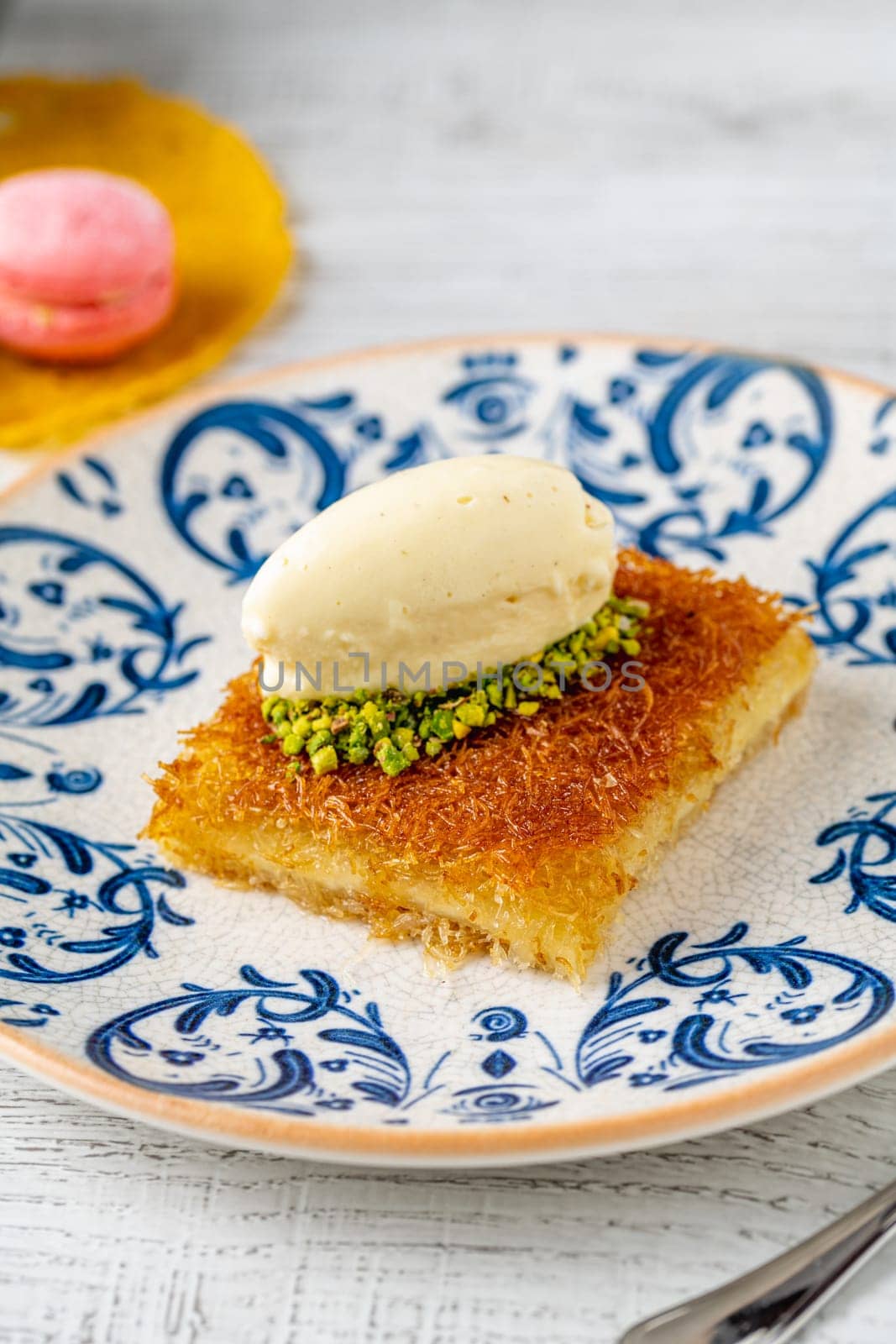 Kunefe with pistachios and ice cream on a porcelain plate on a wooden table by Sonat