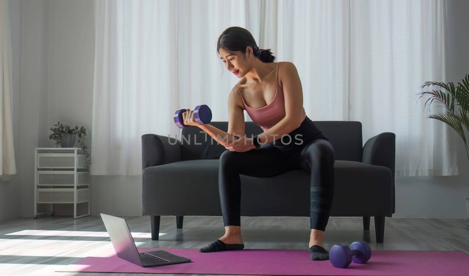 Young woman exercising in front of laptop Wear a sports bar outfit. Do yoga and lift dumbbells on the exercise mat..