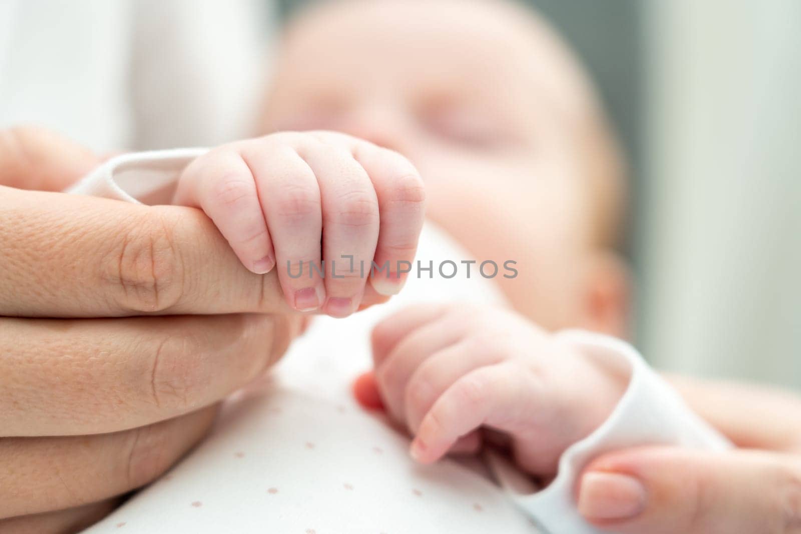 Close-up of a peaceful newborn embracing mother's hand in sleep, reflecting comfort and attachment