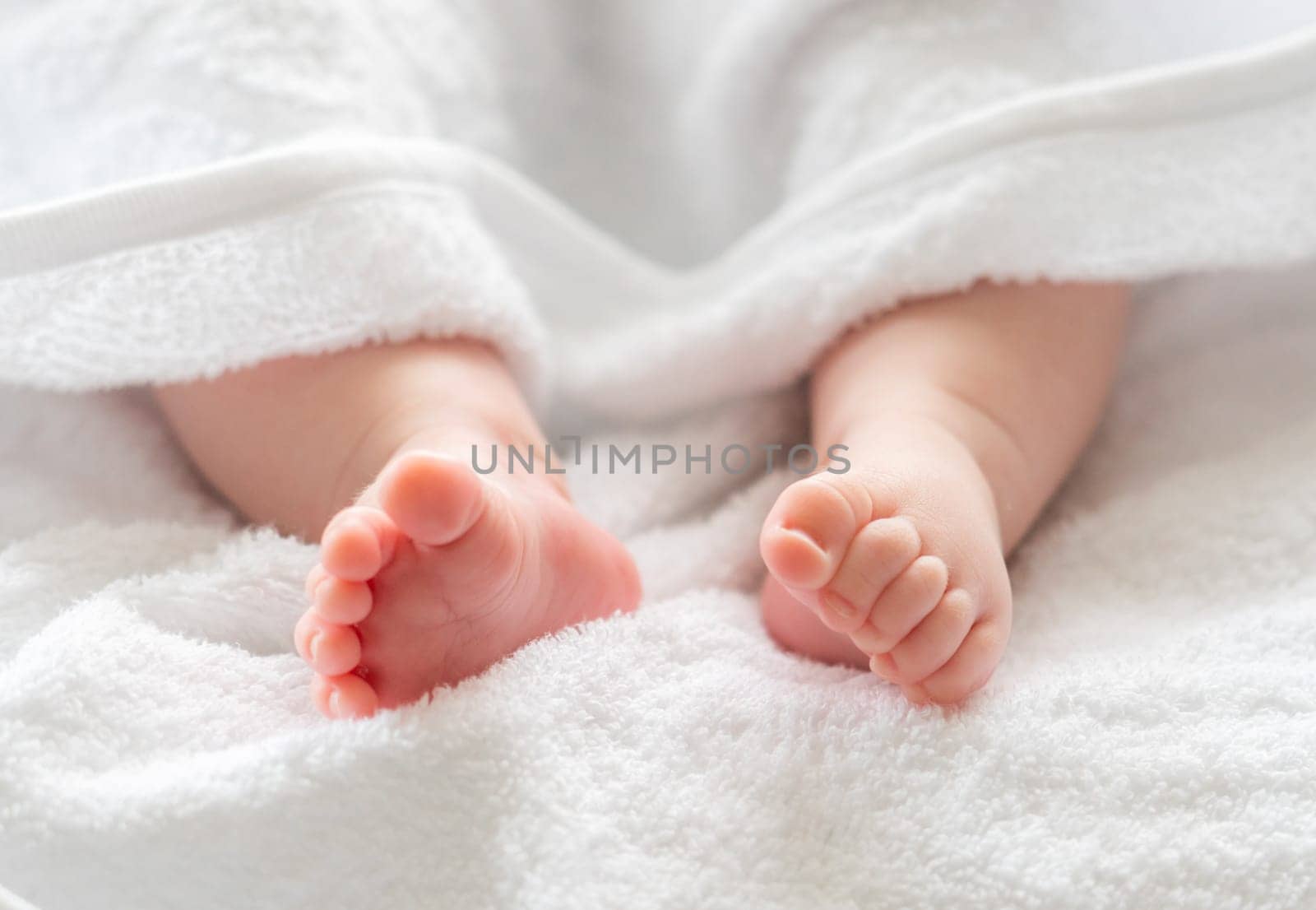 After a comforting bath, an infant child's feet and legs subtly appear from beneath the gentle protection of a white towel