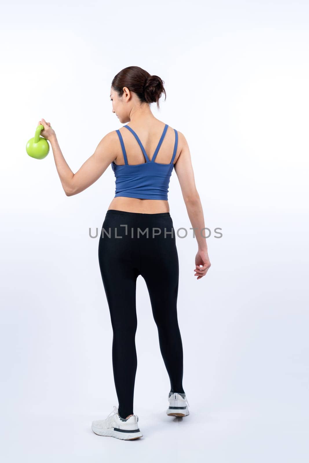 Vigorous energetic woman doing kettlebell weight lifting exercise on isolated background. Young athletic asian woman strength and endurance training session as body workout routine.