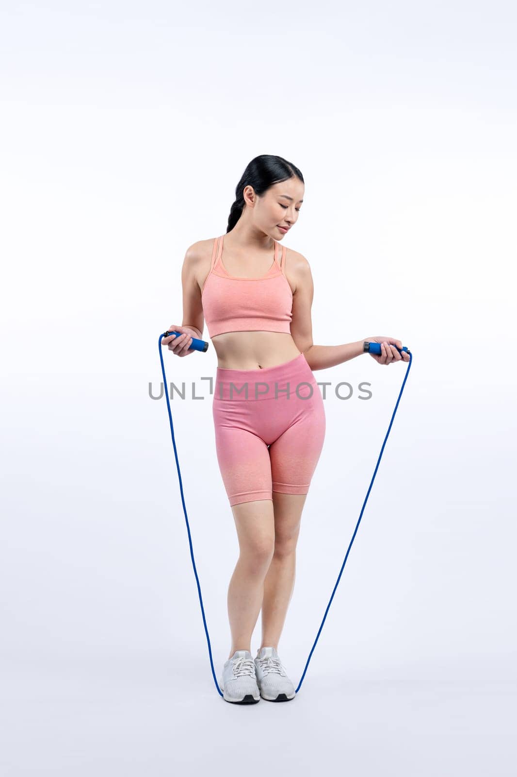 Young energetic asian woman in sportswear with jumping or skipping robe posing portrait in studio shot on isolated background. Cardio exercise tool and healthy body care lifestyle. Vigorous