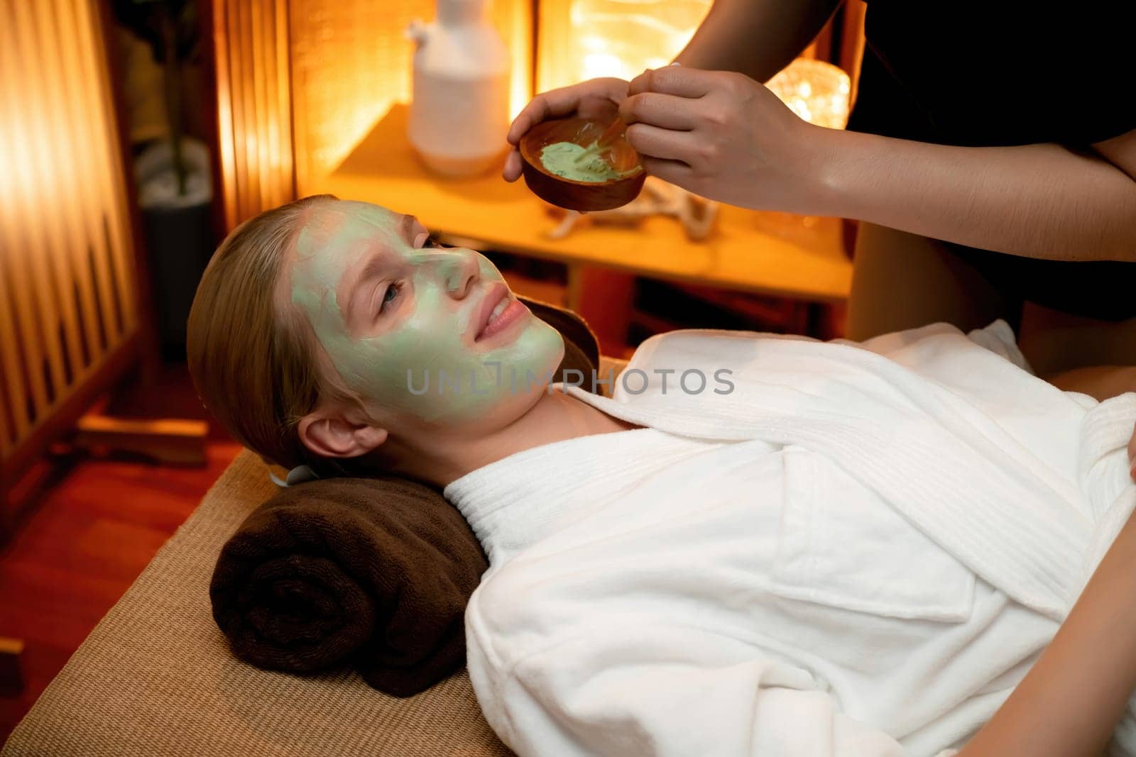 Serene ambiance of spa salon, woman customer indulges in rejuvenating with luxurious face cream massage with warm lighting candle. Facial skin treatment and beauty care concept. Quiescent