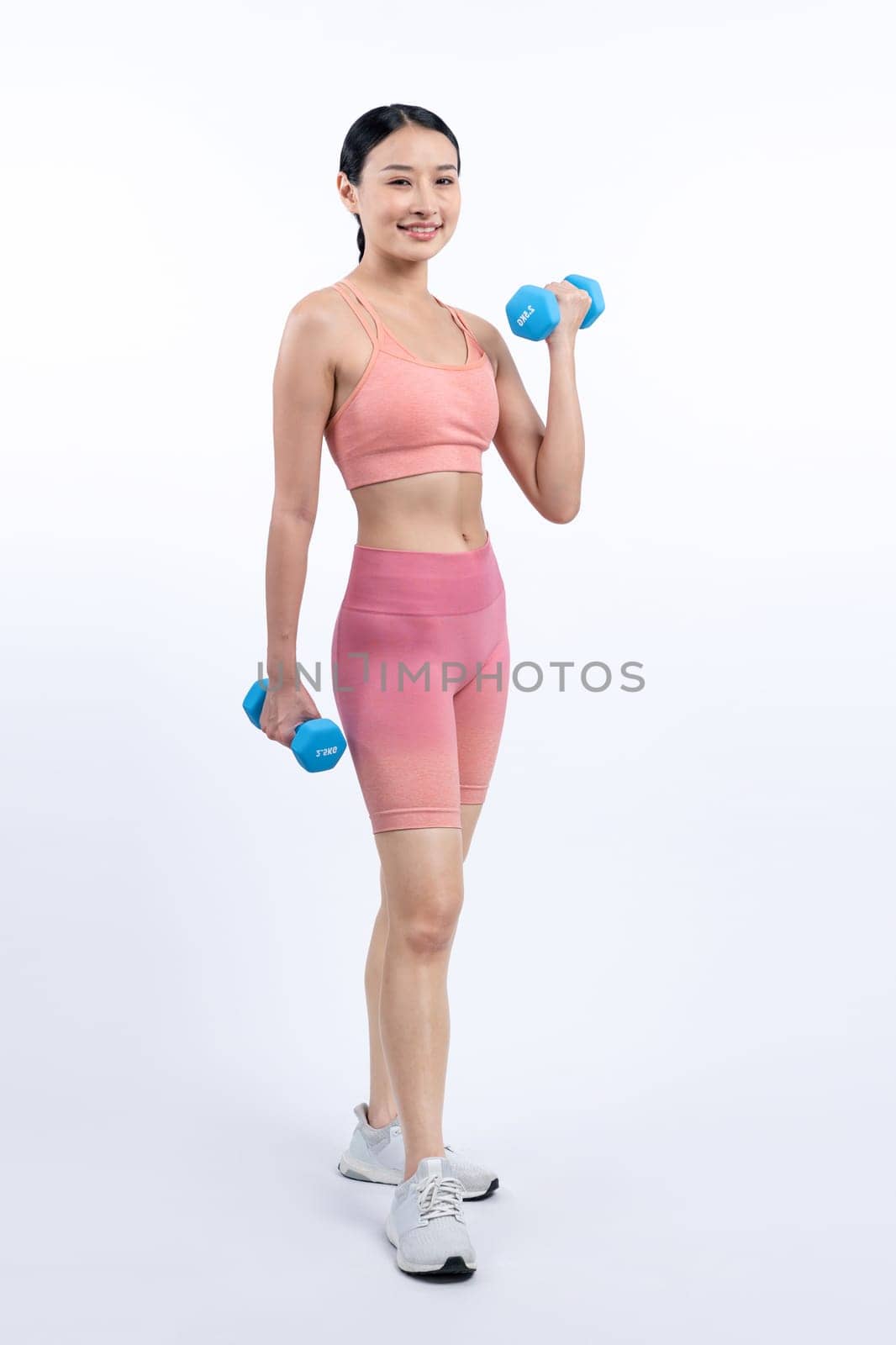 Vigorous energetic woman doing dumbbell weight lifting exercise on isolated background. Young athletic asian woman strength and endurance training session as body workout routine.