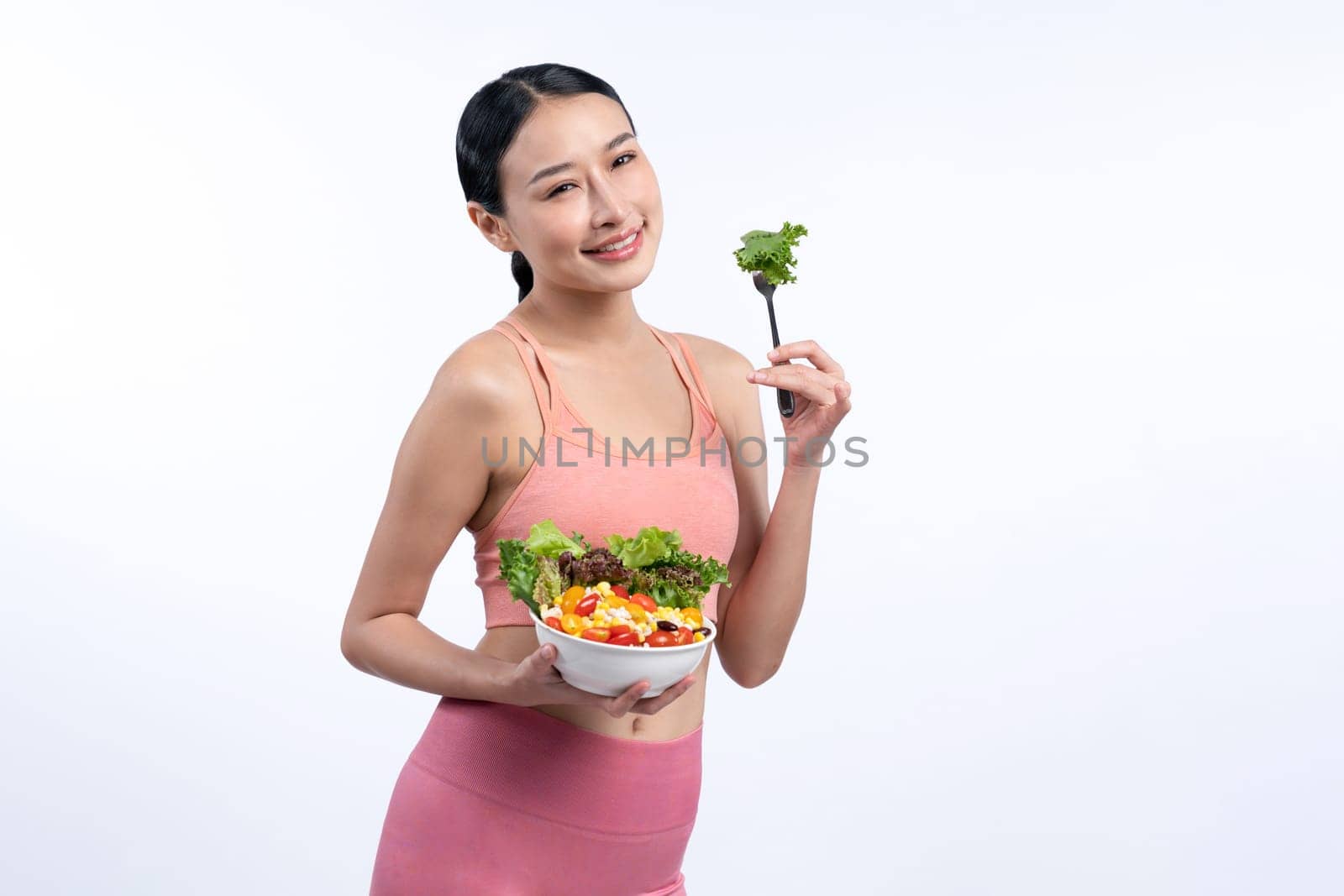 Young sporty Asian woman in sportswear holding salad bowl fill with vibrant of fruit and vegetable. Natural youthful and fit body lifestyle with balance nutrition on isolated background. Vigorous