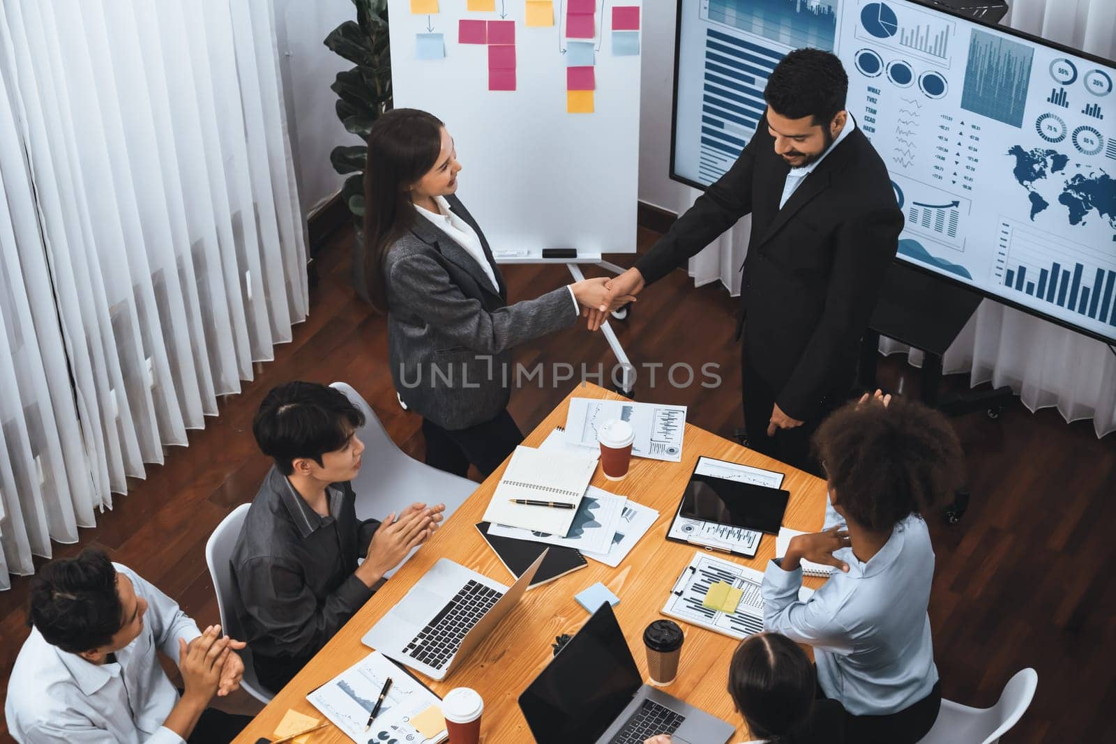 Diverse coworker celebrate with handshake and teamwork in corporate workplace. Happy business people united by handshaking after successful meeting or business presentation on data analysis. Concord