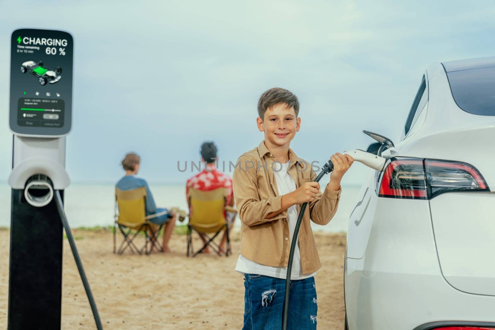 Family vacation trip traveling by the beach with electric car, little boy recharge EV car while his family enjoy seascape beach. Family trip with alternative energy and eco-friendly car. Perpetual