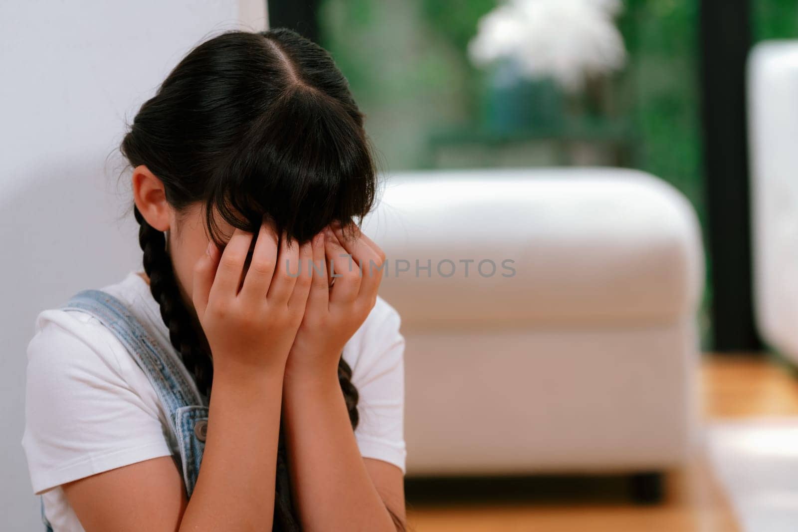 Sad little girl sitting alone in living room crying, feeling lonely. Young girl experiencing social isolation punishment or neglect from parent led to anxiety and traumatic in childhood. Synchronos