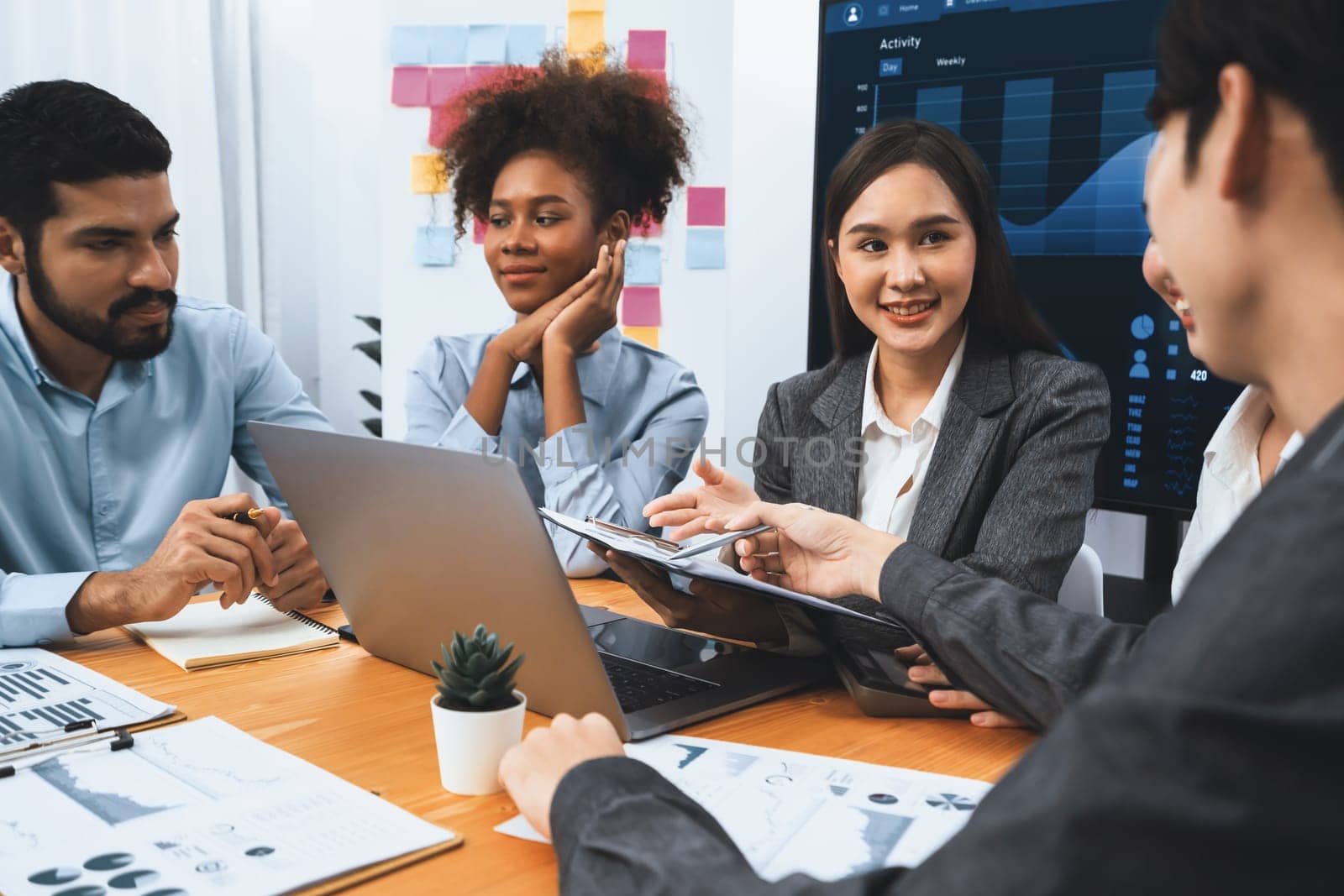 Multiracial analyst team use BI dashboard data to analyze financial report on meeting table. Group of diverse business people utilize data analysis by FIntech for success business marketing. Concord