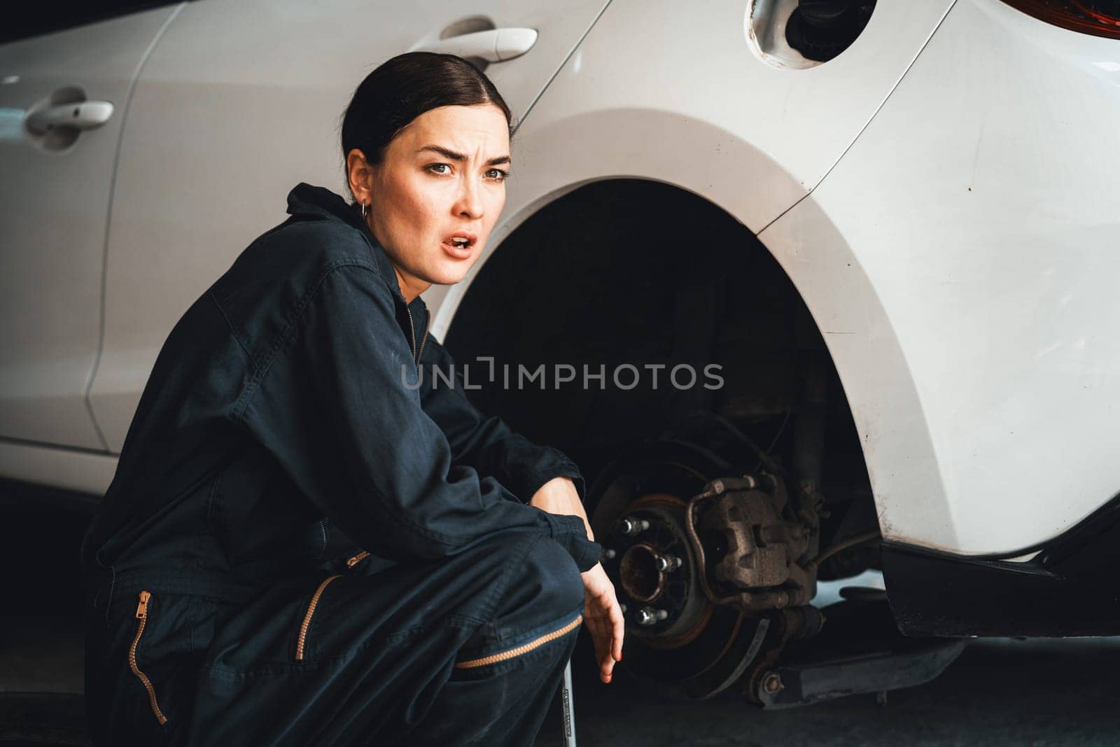 Hardworking female mechanic changing car wheel in auto repair workshop. Oxus by biancoblue