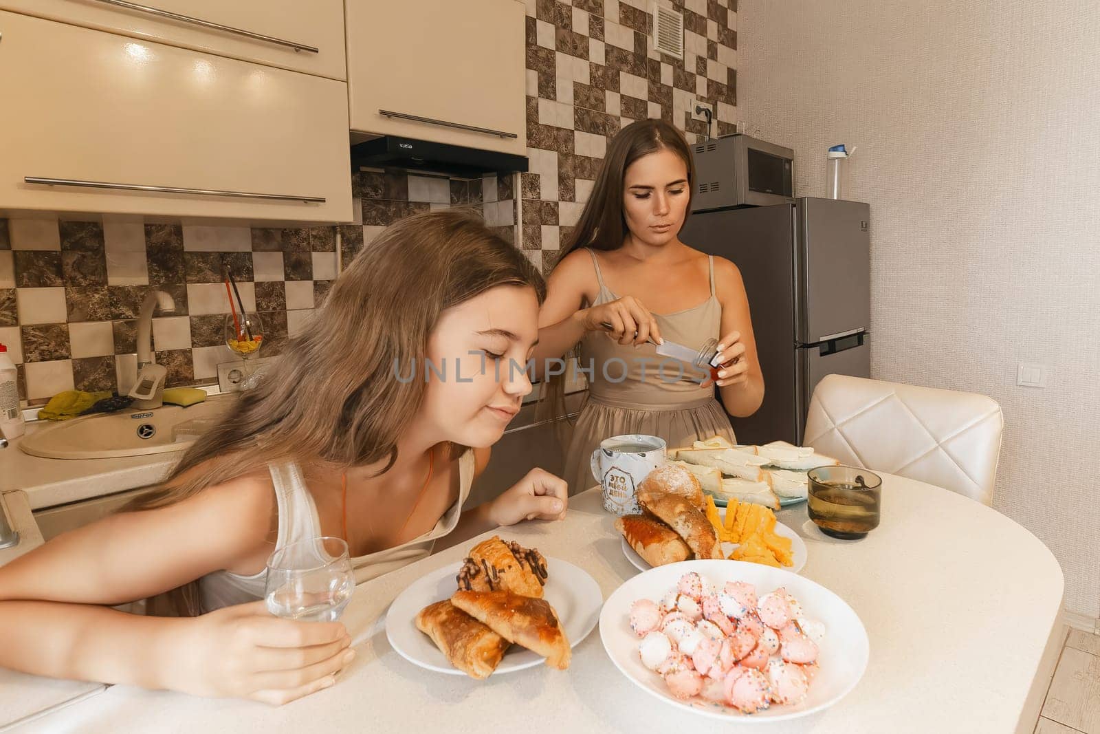 A woman is eating a sandwich and a girl is looking at her. The girl is wearing a white dress
