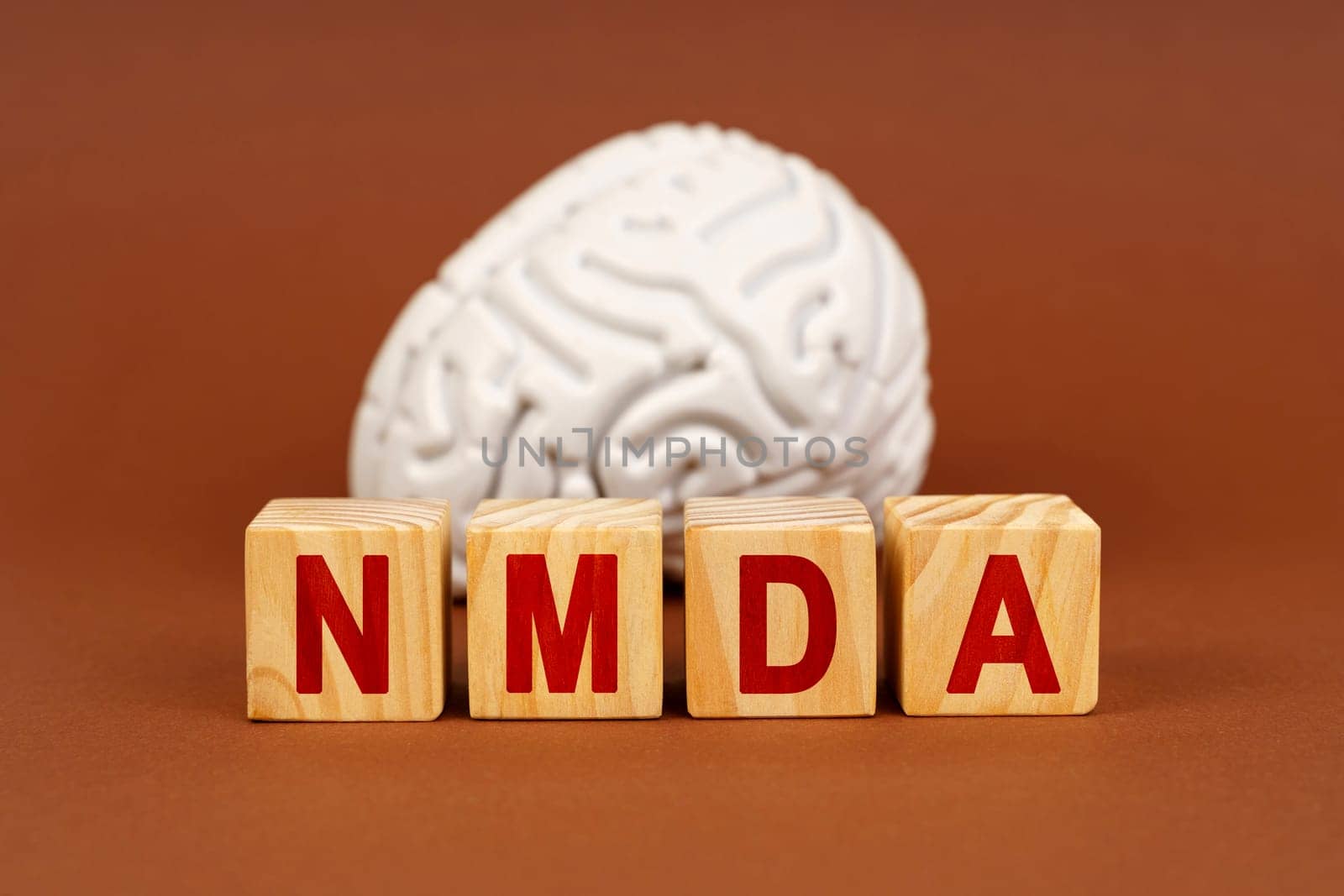 Cubes spell out NMDA in front of a stylized brain, symbolizing the connection between this compound and neural processes.
