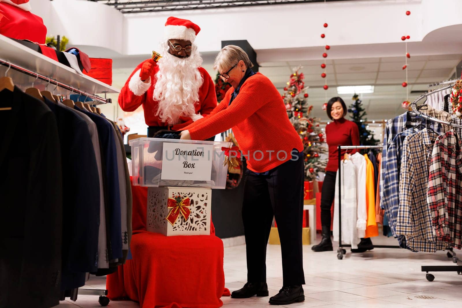 Clients donating clothes for charity at shopping center, putting items in donation box to people in need. Santa claus and buyers spreading kindness and holiday spirit around christmas eve.