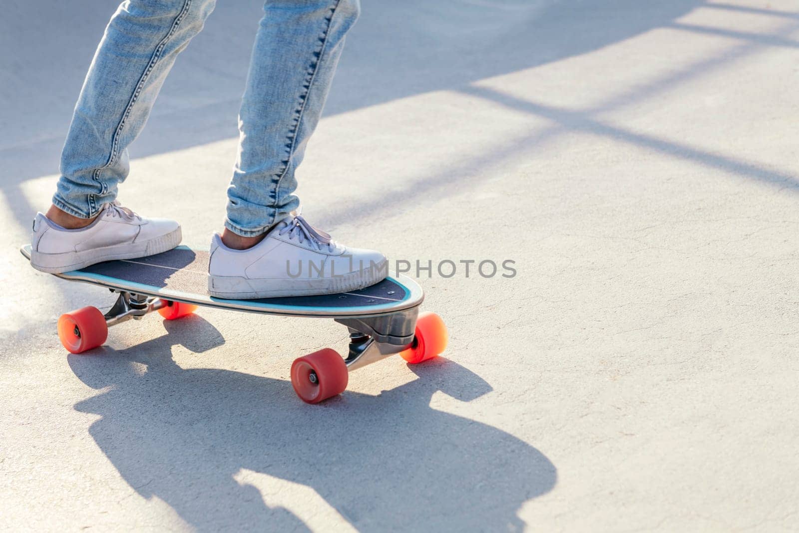 unrecognizable stylish skater in jeans and sneakers standing on skateboard in skatepark on sunny day in summer