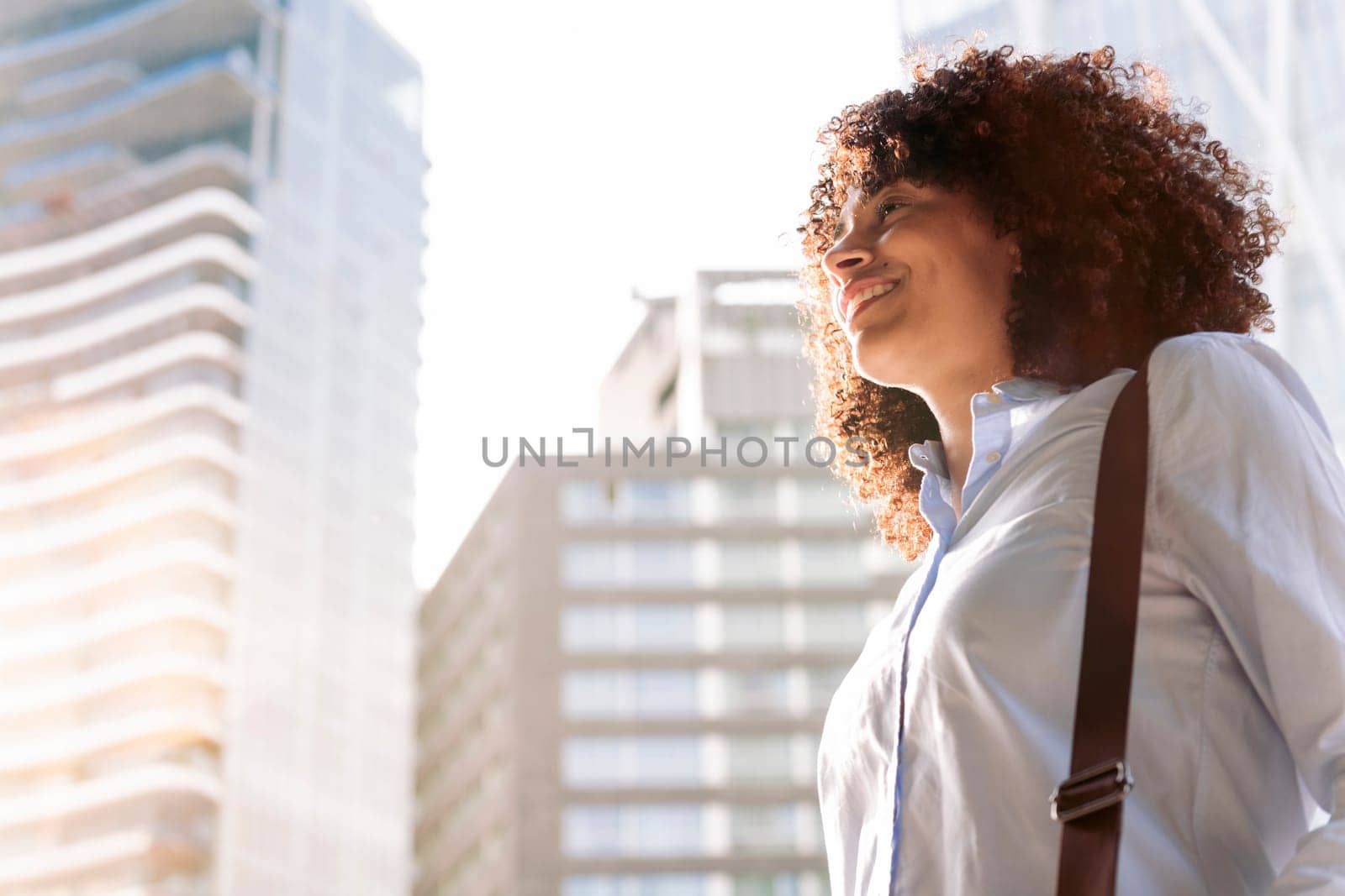 portrait of a smiling female entrepreneur in smart casual outfit walking along street in megalopolis and looking away