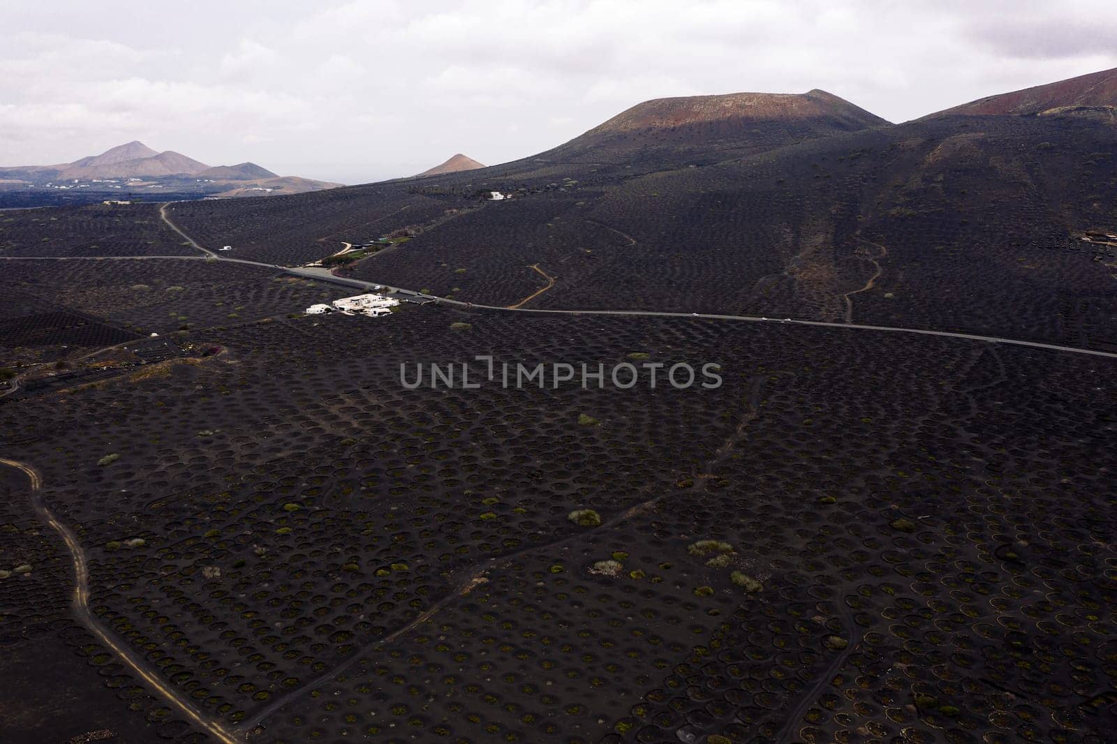 drone view of vines growing in pit against high dry mountains in Geria, Lanzarote at Canary Islands, Spain, concept of viticulture and traditional agriculture