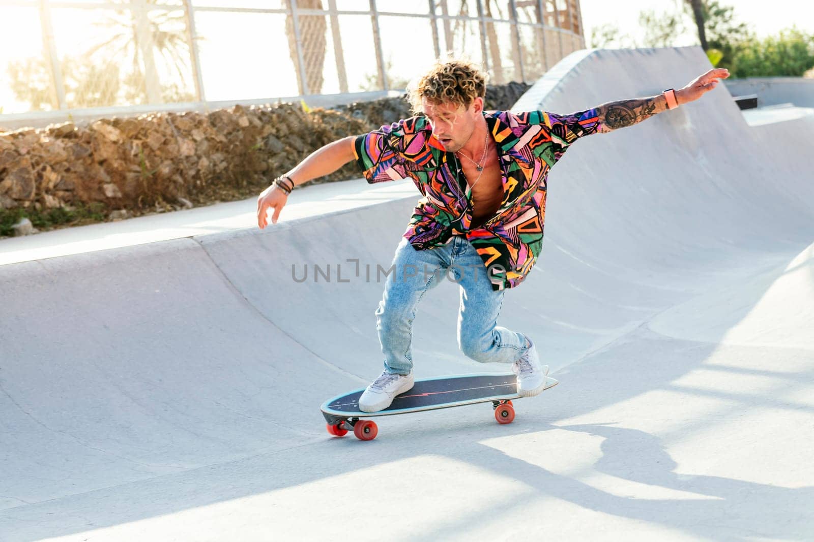 full body of funky young male skateboarder in trendy colorful shirt and jeans performing trick on concrete ramp while practicing skills in skatepark