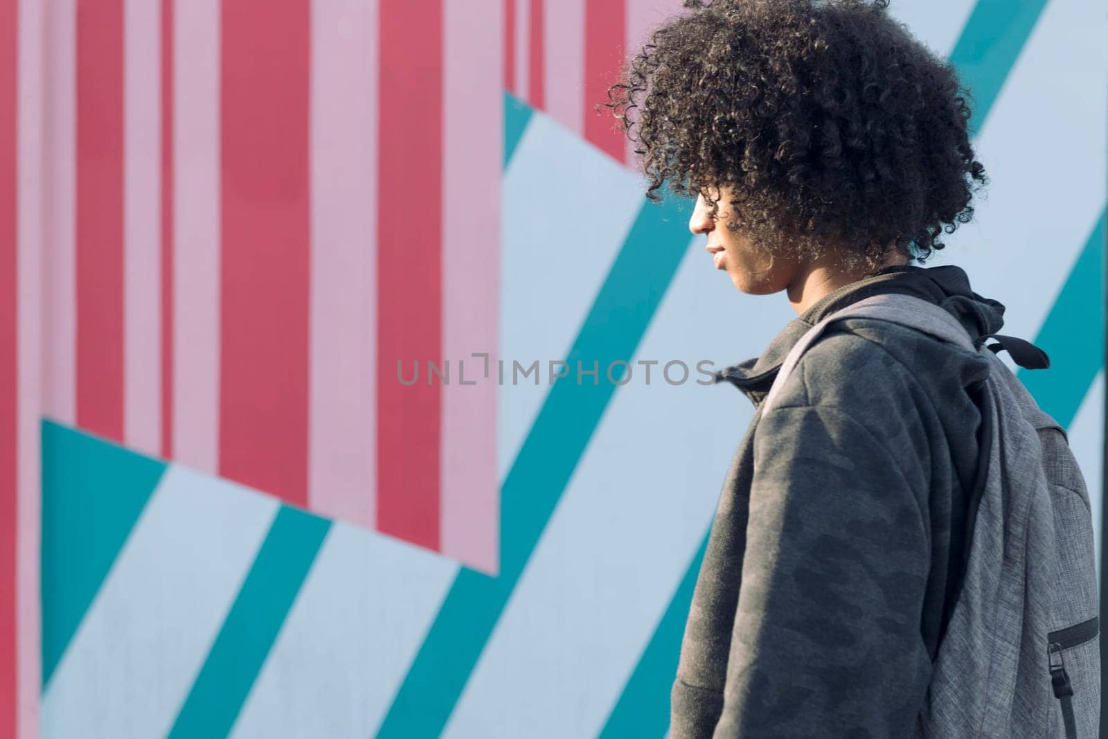 unrecognizable curly haired african american teenager dressed in casual clothes walking on the street in front of colorful wall, young lifestyle concept