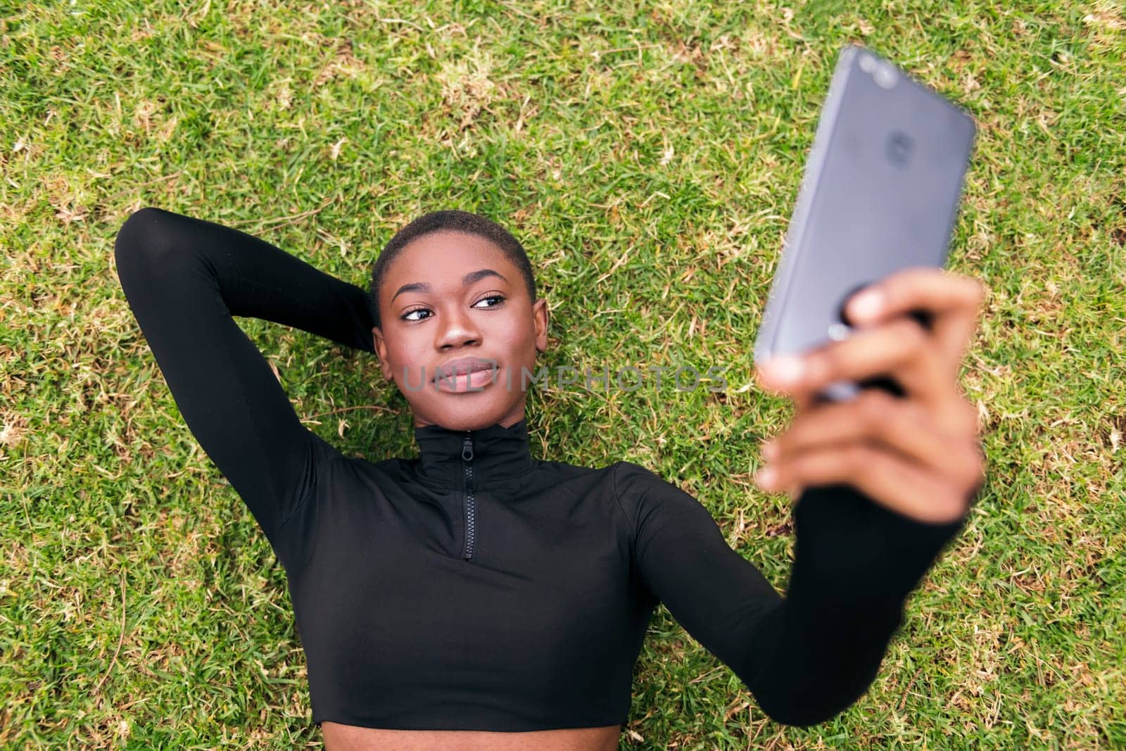 young african american woman lying on the grass in a park smiling happy taking selfie photo on mobile phone, concept of technology and modern lifestyle