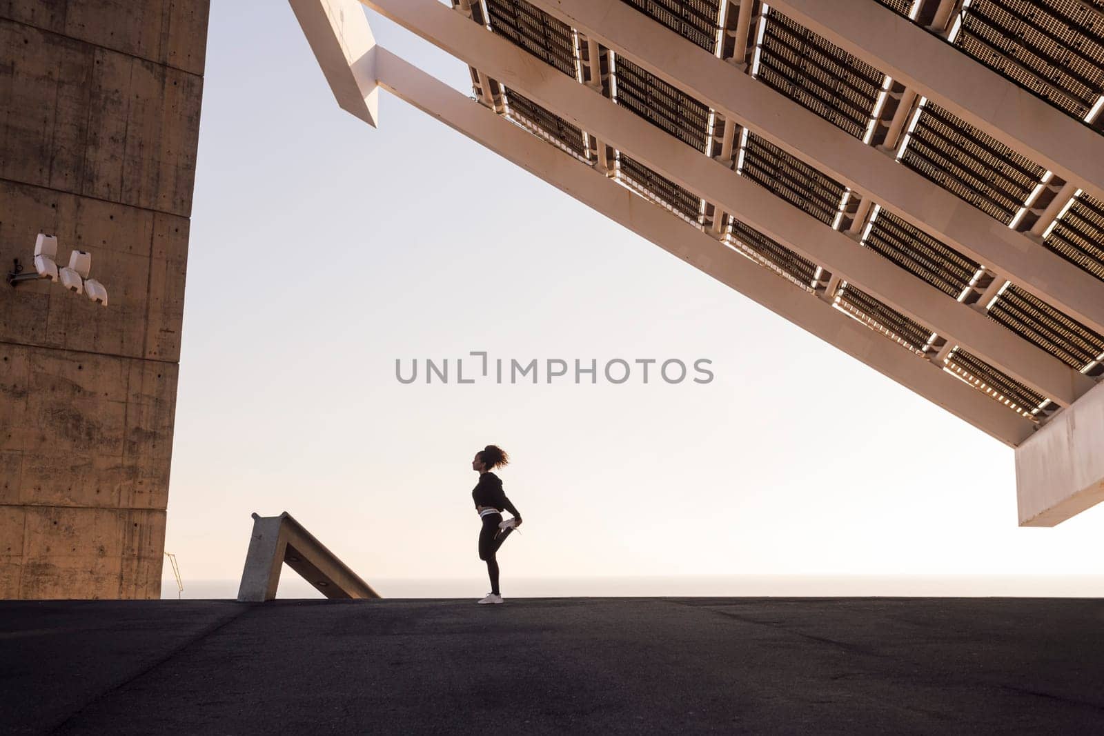 african american female athlete stretching during training under modern house while looking away in city, concept of urban sports and healthy lifestyle