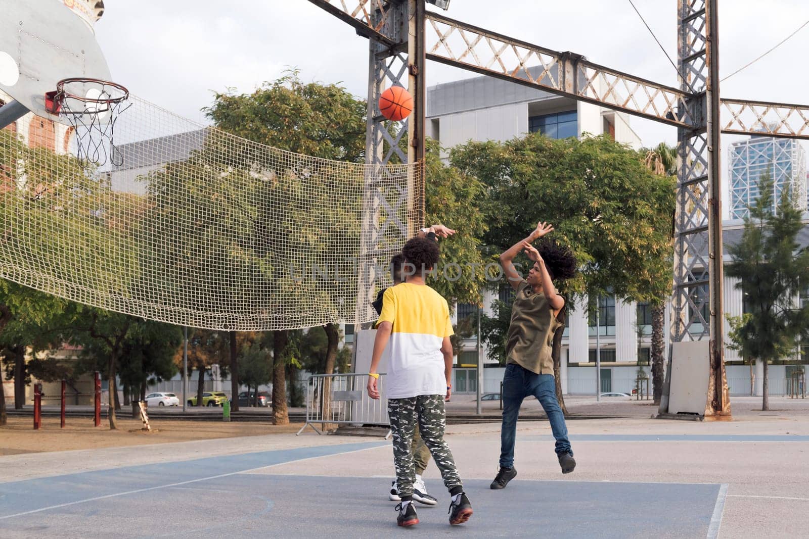three focused multiethnic teen friends having fun playing basketball on sports ground in city park, concept of youth and urban lifestyle