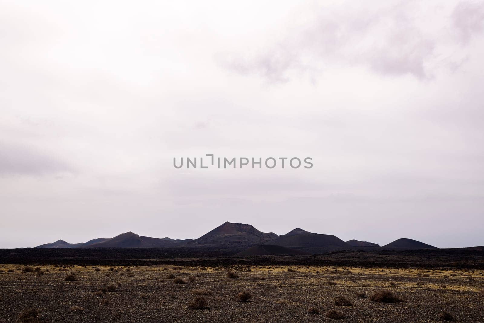 scenery view of volcano Cuervo and rough mountains under cloudy sky in Tinajo, Lanzarote at Canary Islands Spain, concept of dry landscape and adventure travel