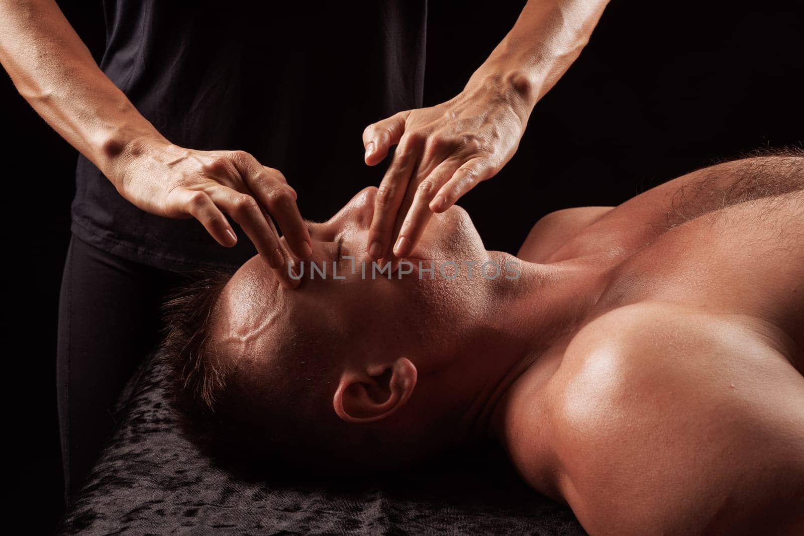 girl masseur doing facial massage to man on dark background close-up, facial skin rejuvenation, relaxation and meditation