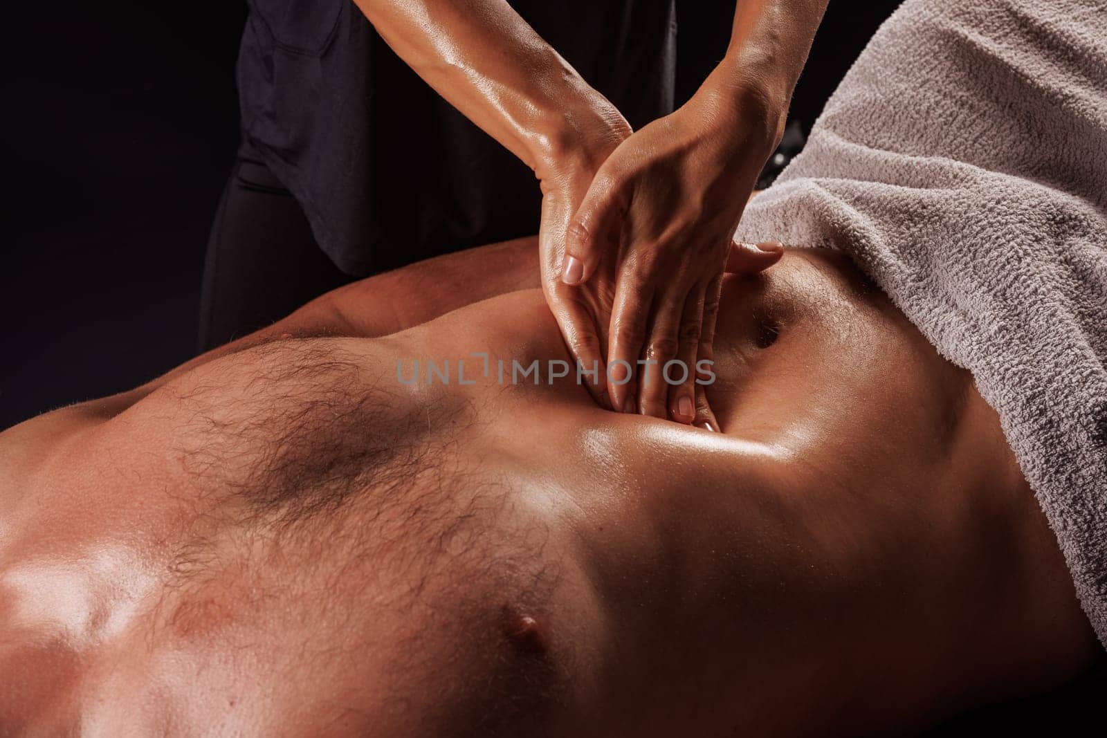 Girl giving abdominal massage to muscular man on dark background, wellness body massage, recovery