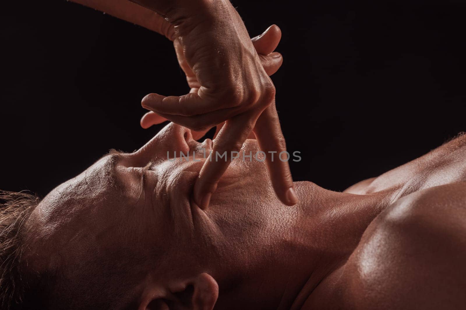 girl masseur doing facial massage to man on dark background close-up, facial skin rejuvenation, relaxation and meditation