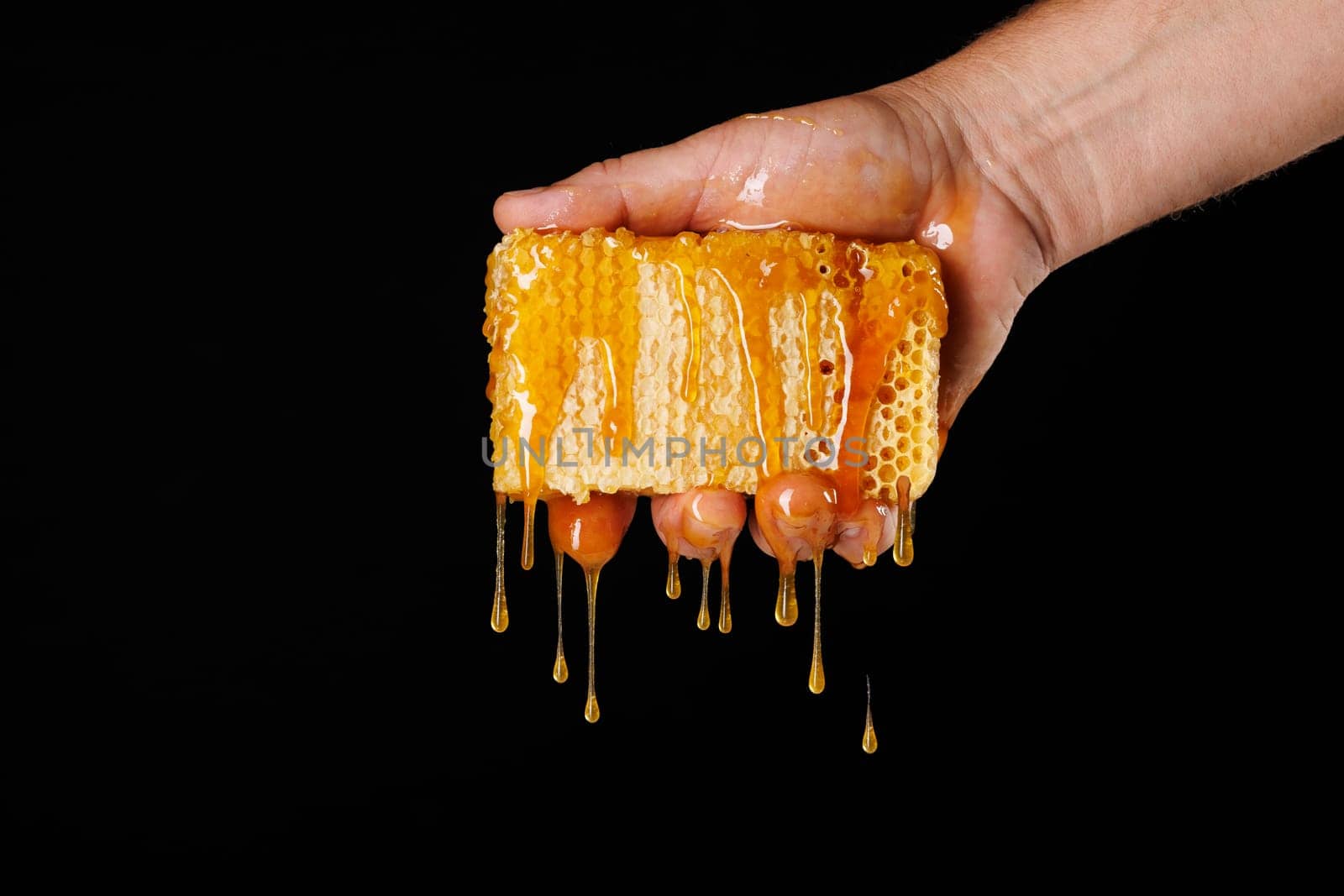 hand squeezing honey from bee honeycomb close-up on dark background, beekeeping concept, beekeeper producing honey