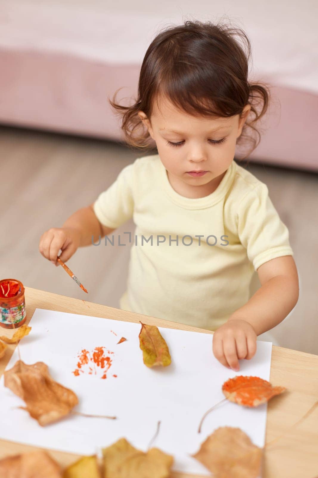 happy little child girl painting autumn leaves. baby girl drawing leaves in yellow and orange paint
